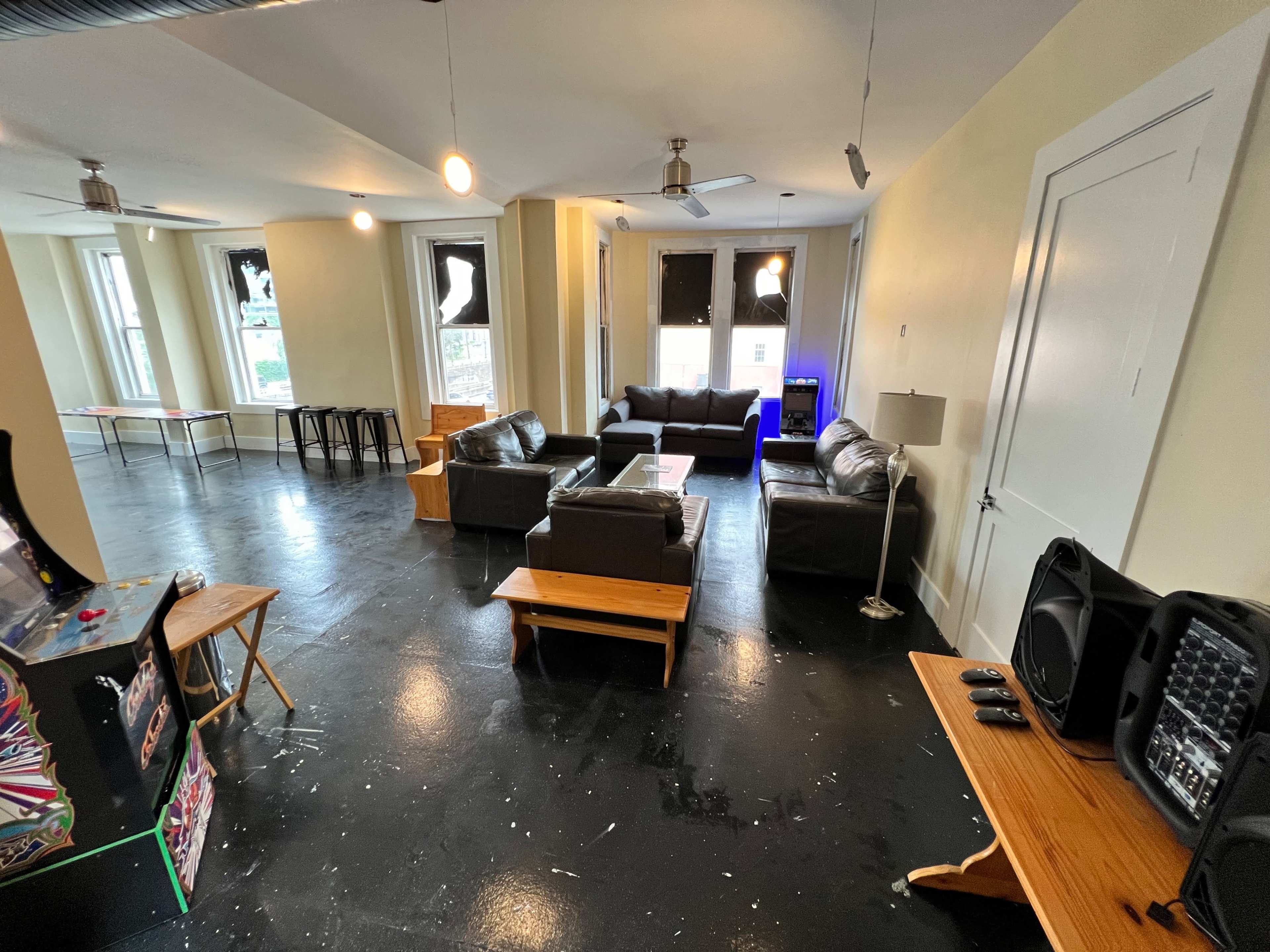 A spacious room with black floors, several seating arrangements, a coffee table, and an arcade game machine in one corner.