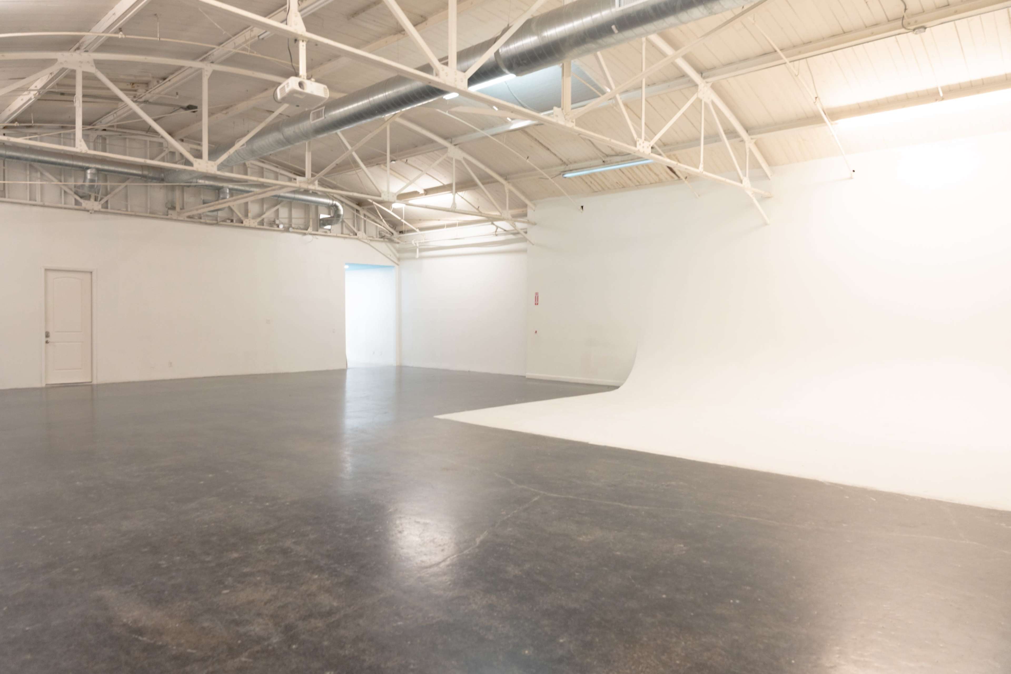 The image shows a spacious, empty studio with white walls and a smooth, curved backdrop, featuring a polished dark floor.