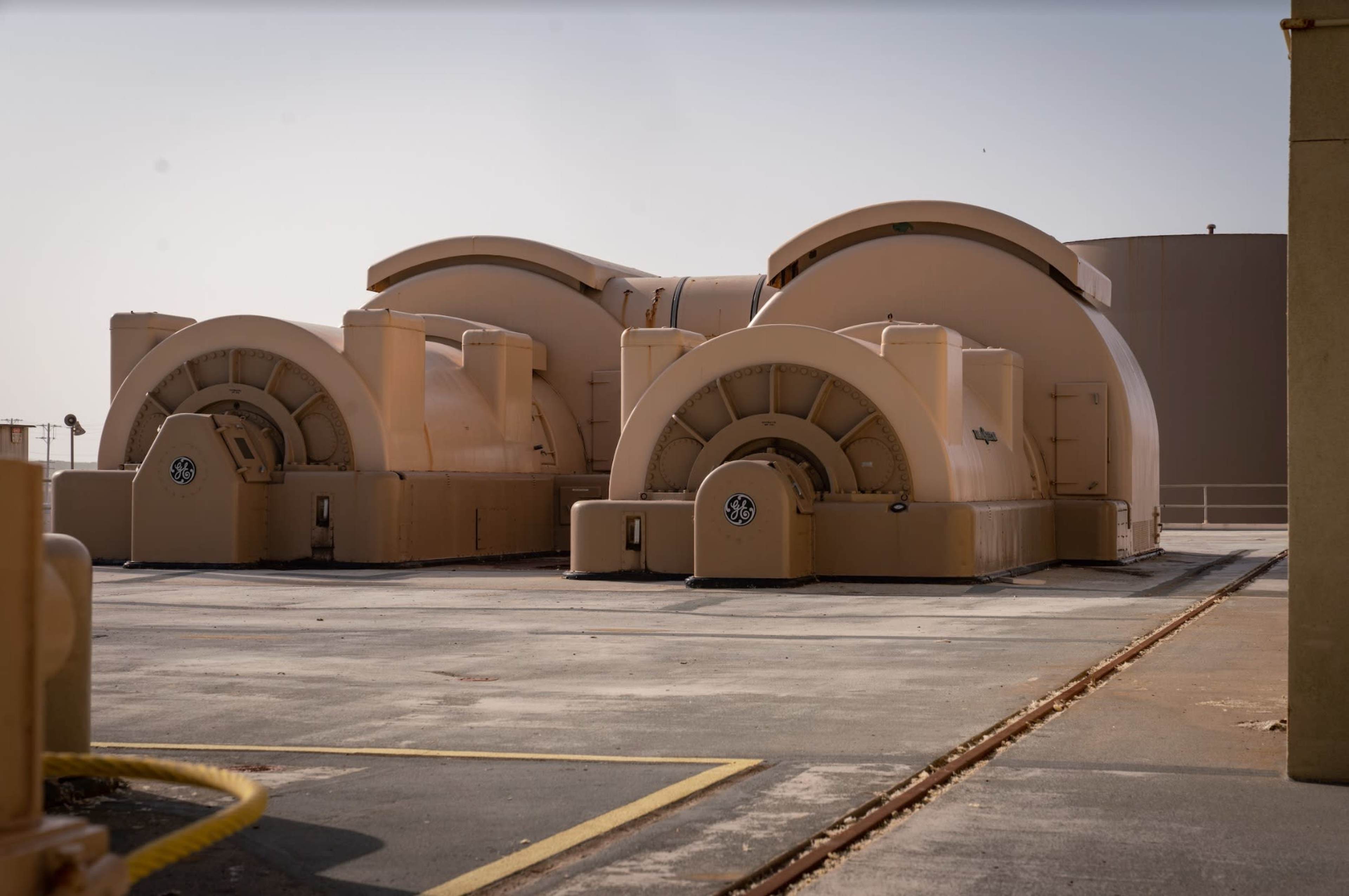 Three large, beige industrial turbines situated on a concrete surface.