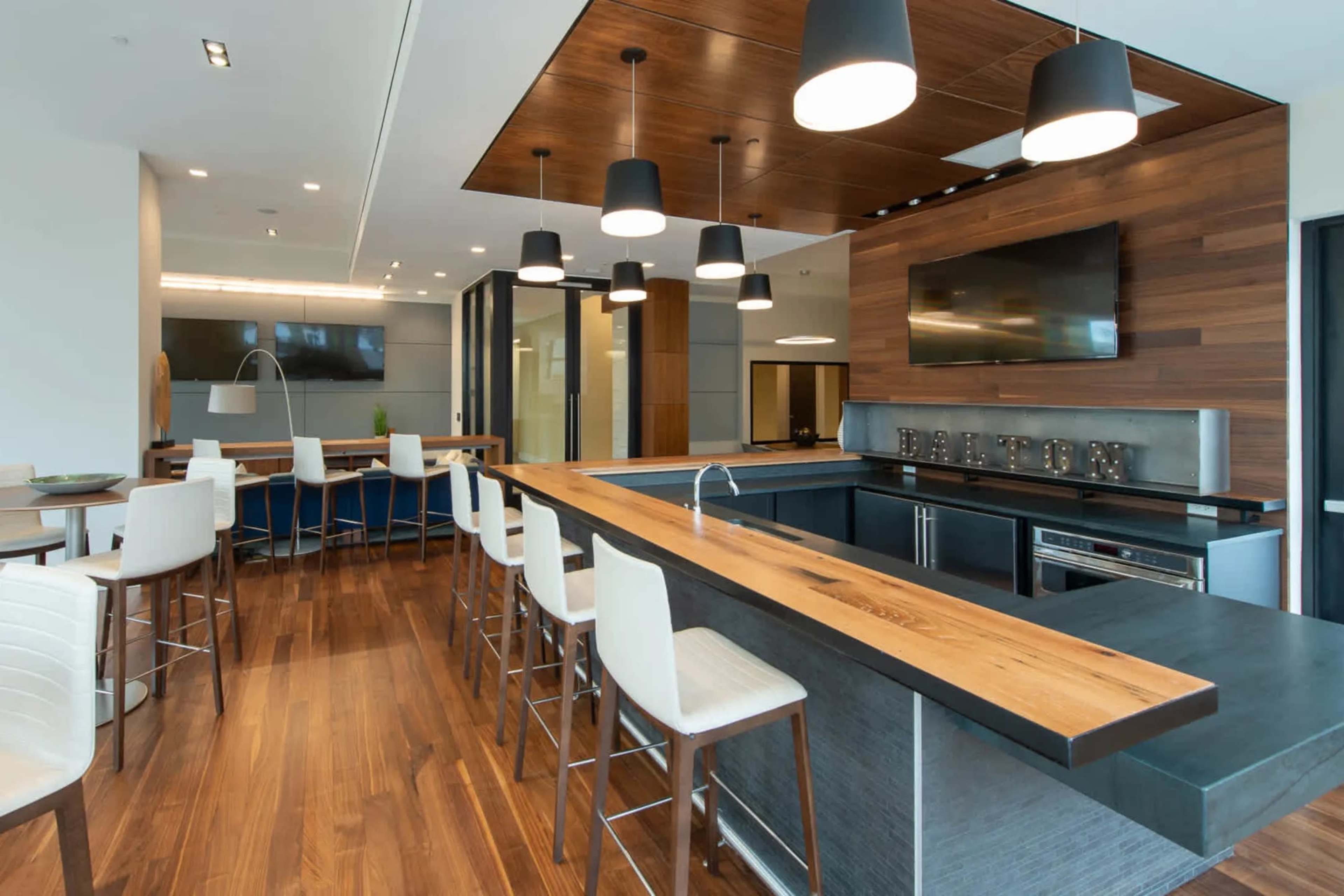 A modern kitchen with a wooden central island, white bar stools, pendant lighting, and dark cabinetry.