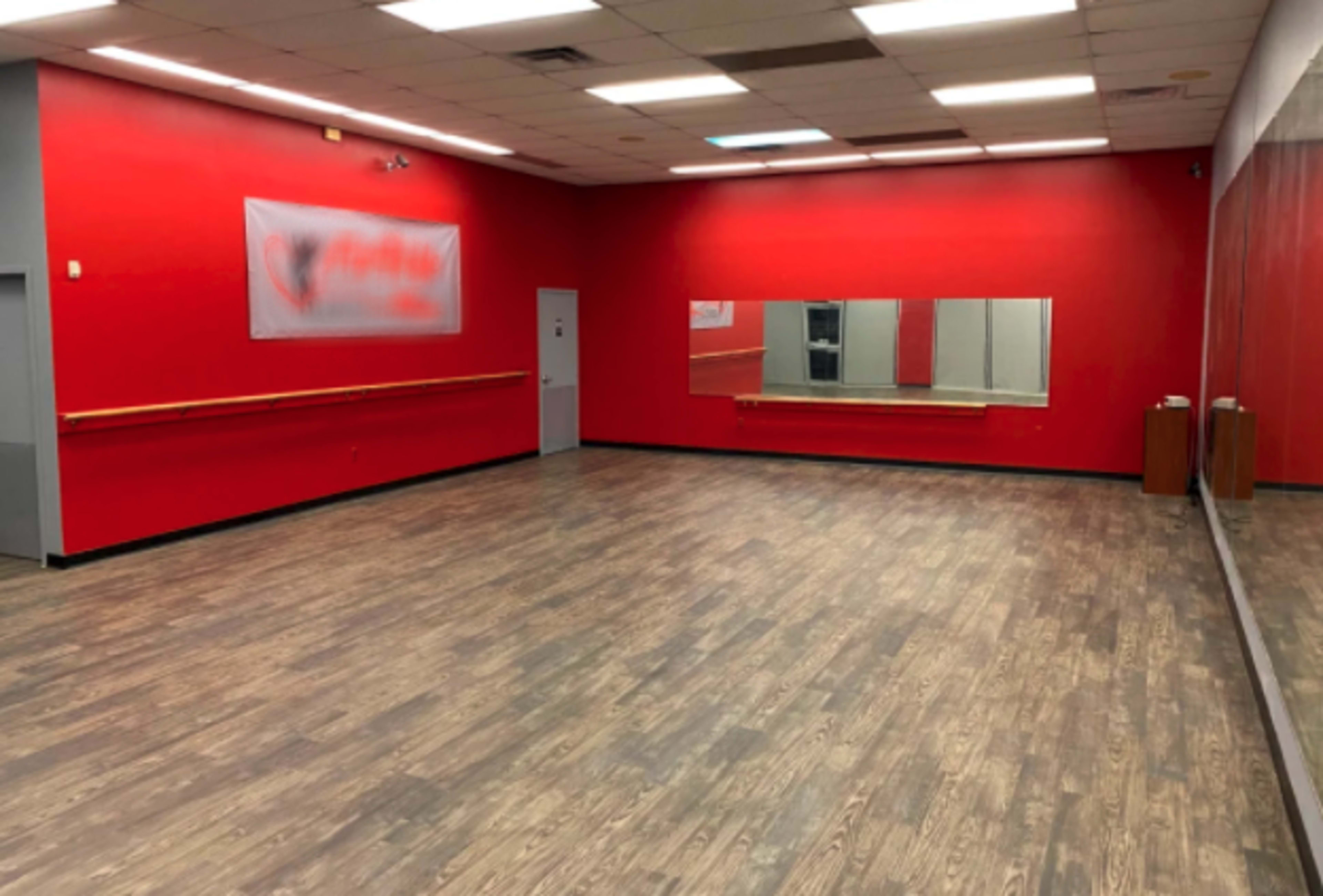 A dance studio features red walls, a large mirror, and wooden flooring.