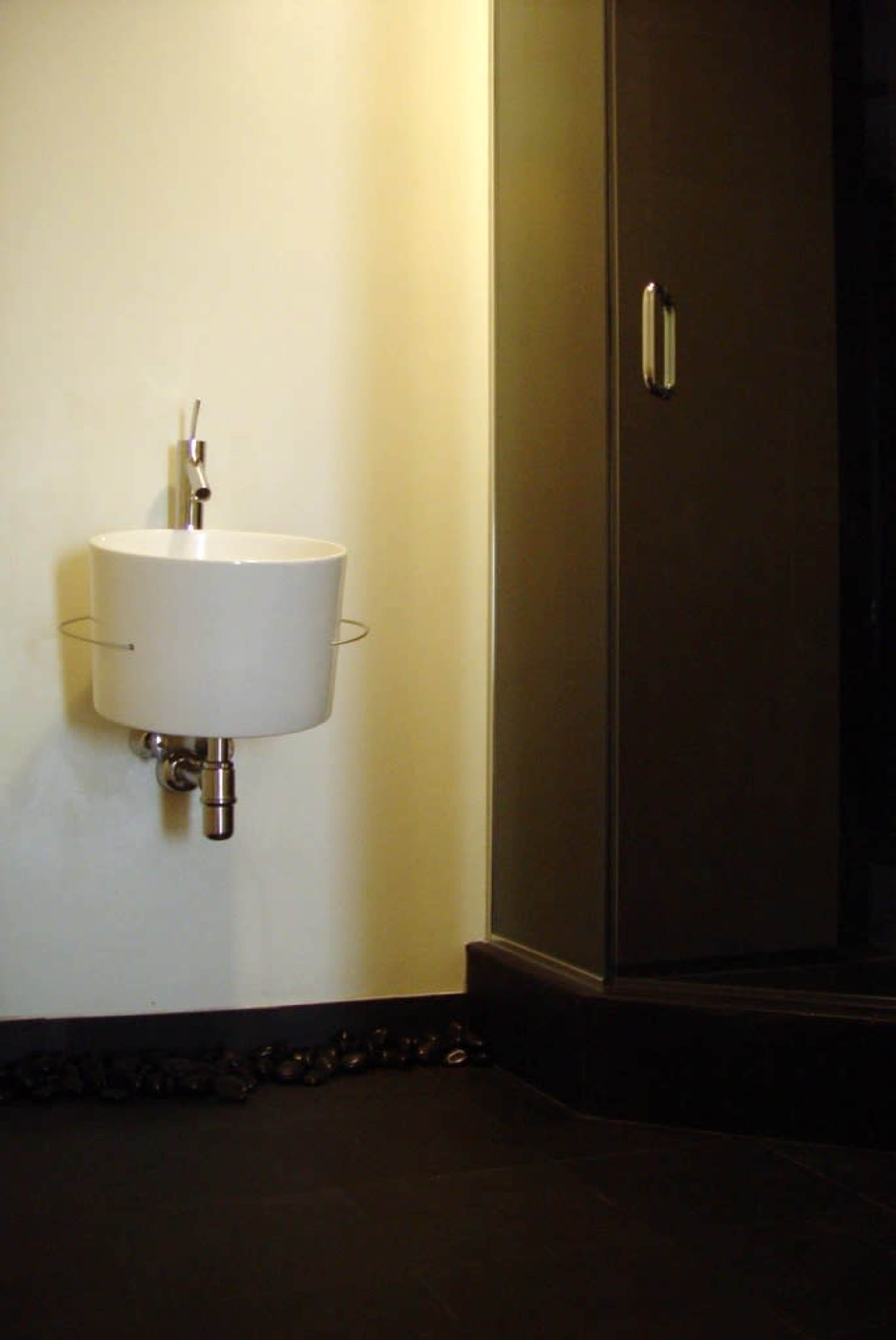 The image shows a modern bathroom featuring a round white sink mounted on the wall next to a glass shower enclosure.