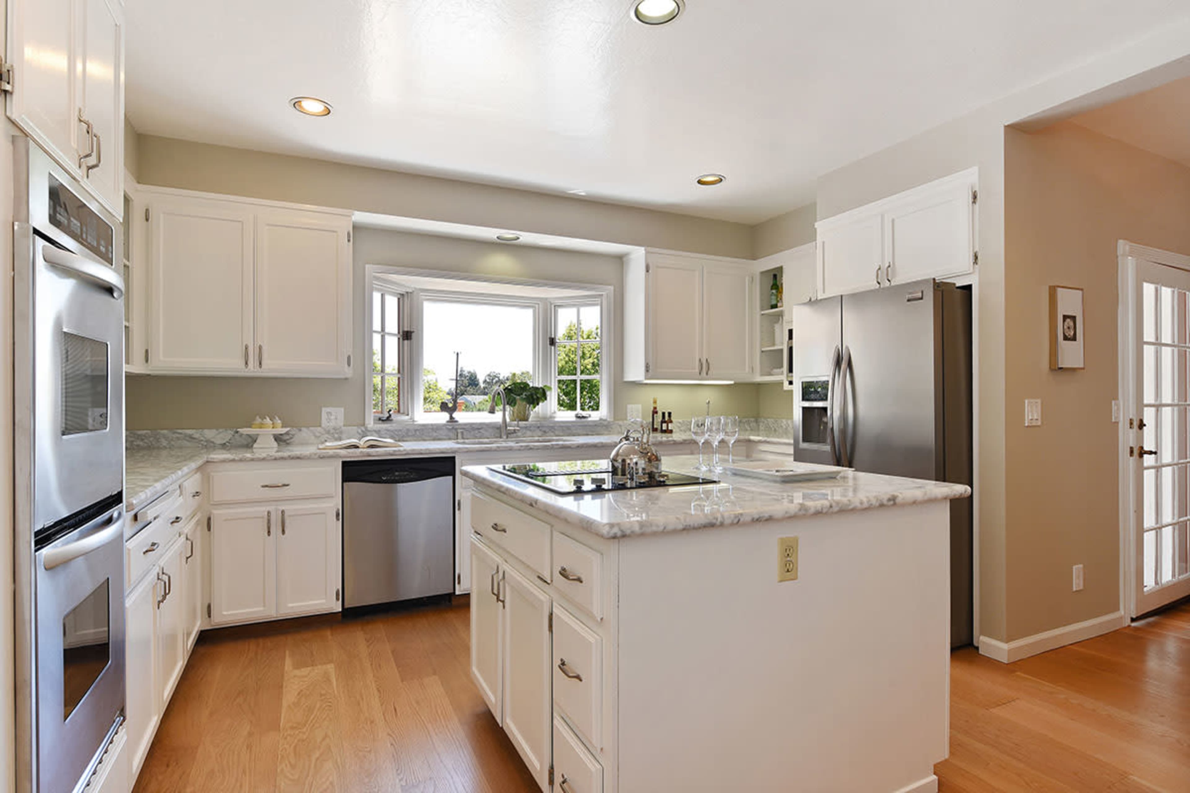 The image shows a modern kitchen with white cabinetry, stainless steel appliances, and a central island with a marble countertop.