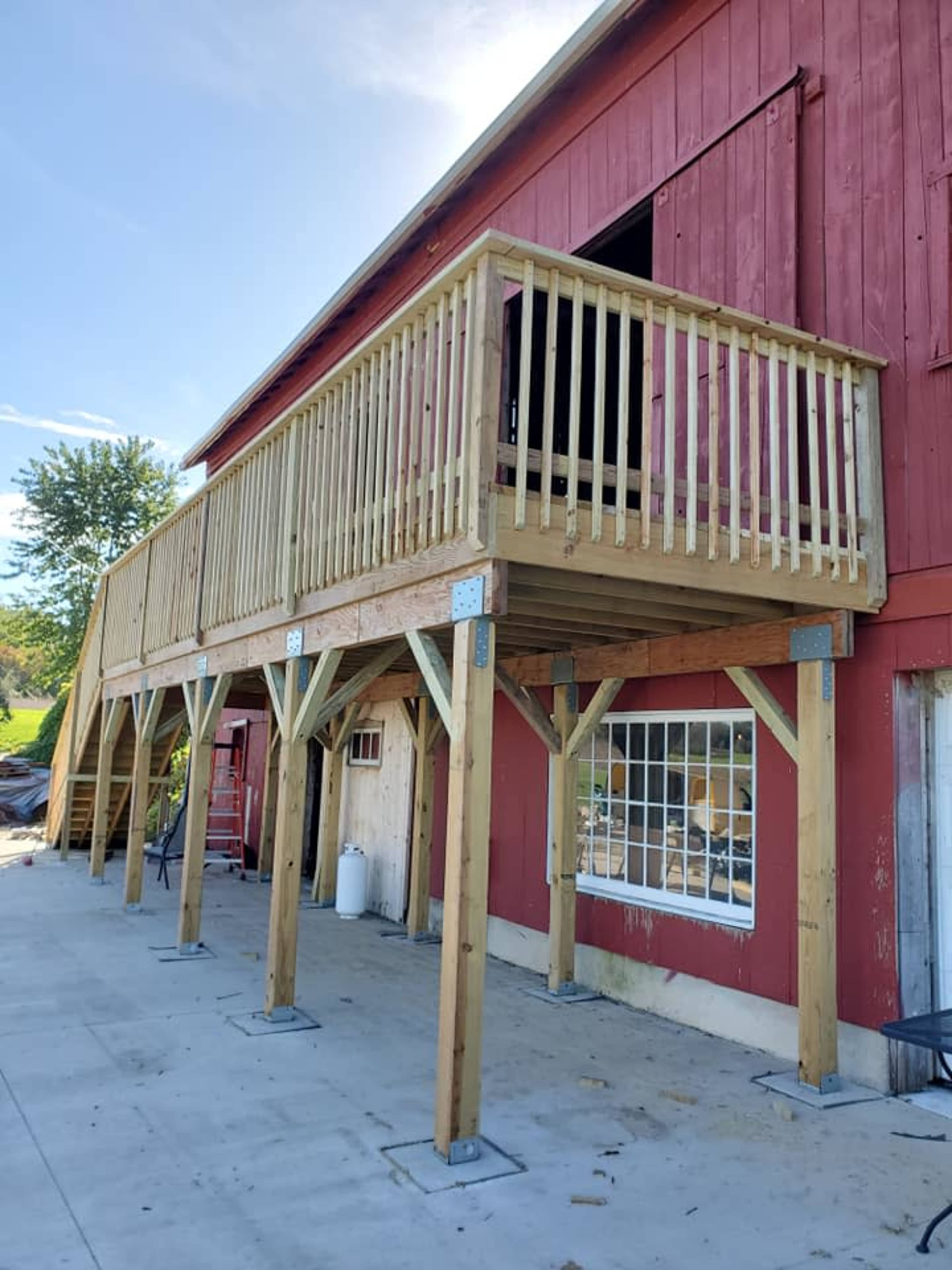 A wooden balcony supported by sturdy posts extends from the side of a red barn.