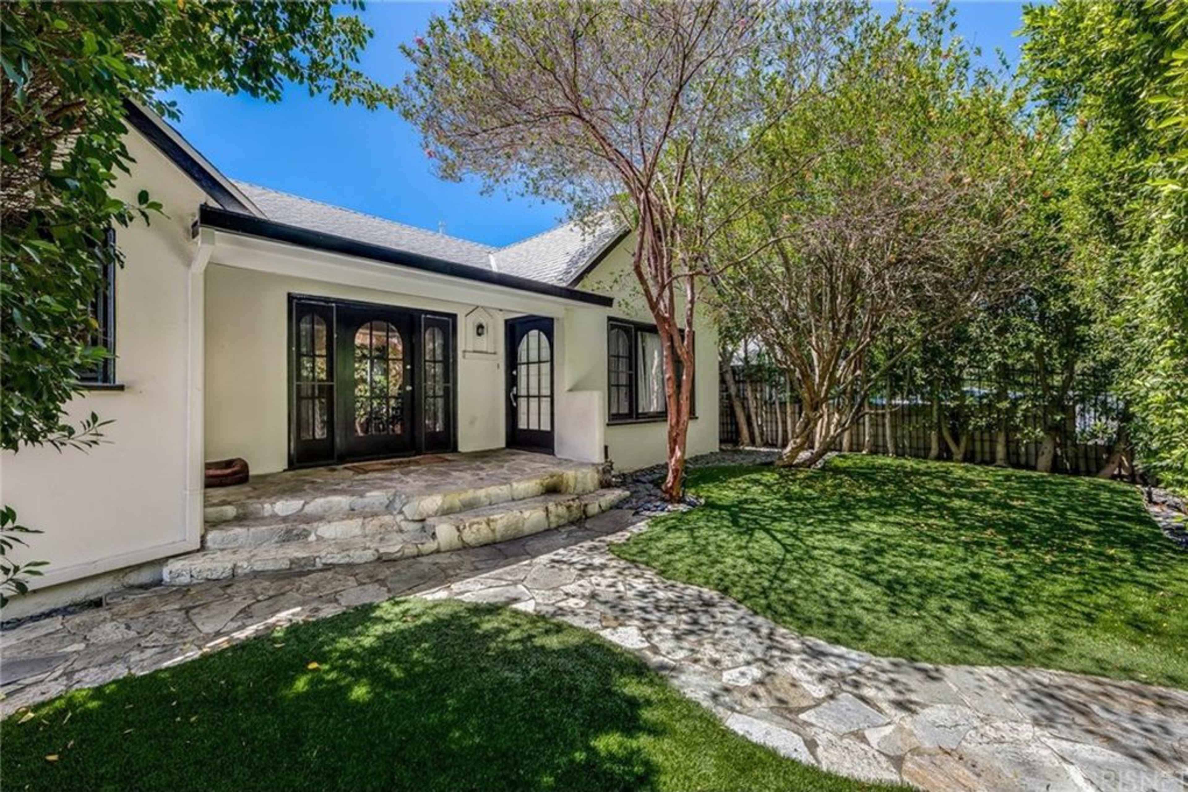 A stone pathway leads to the entrance of a house with a landscaped yard and surrounding trees.