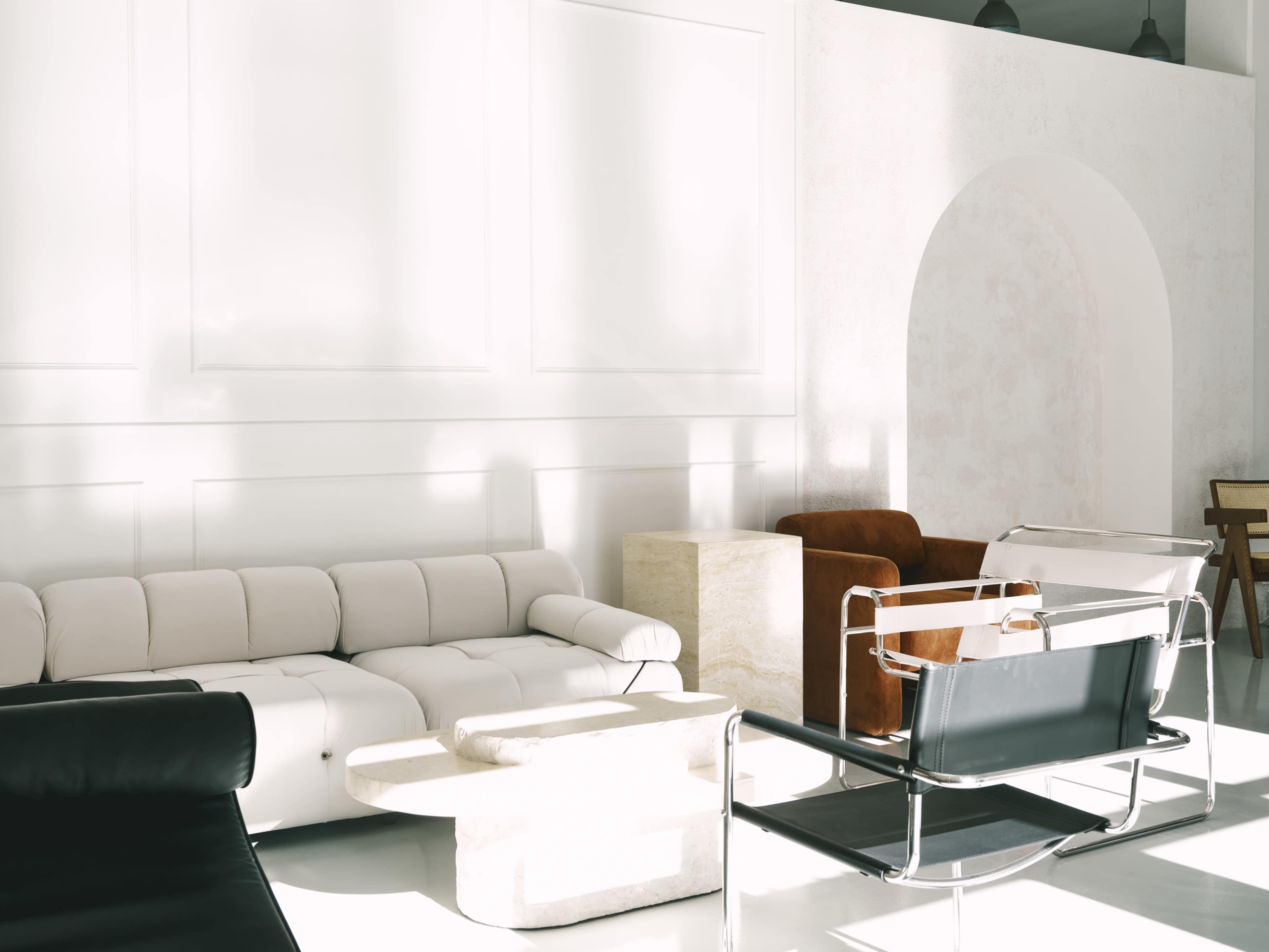 The image depicts a modern interior living space with a combination of minimalist furniture, including a white couch, a black chair, and a stone table.
