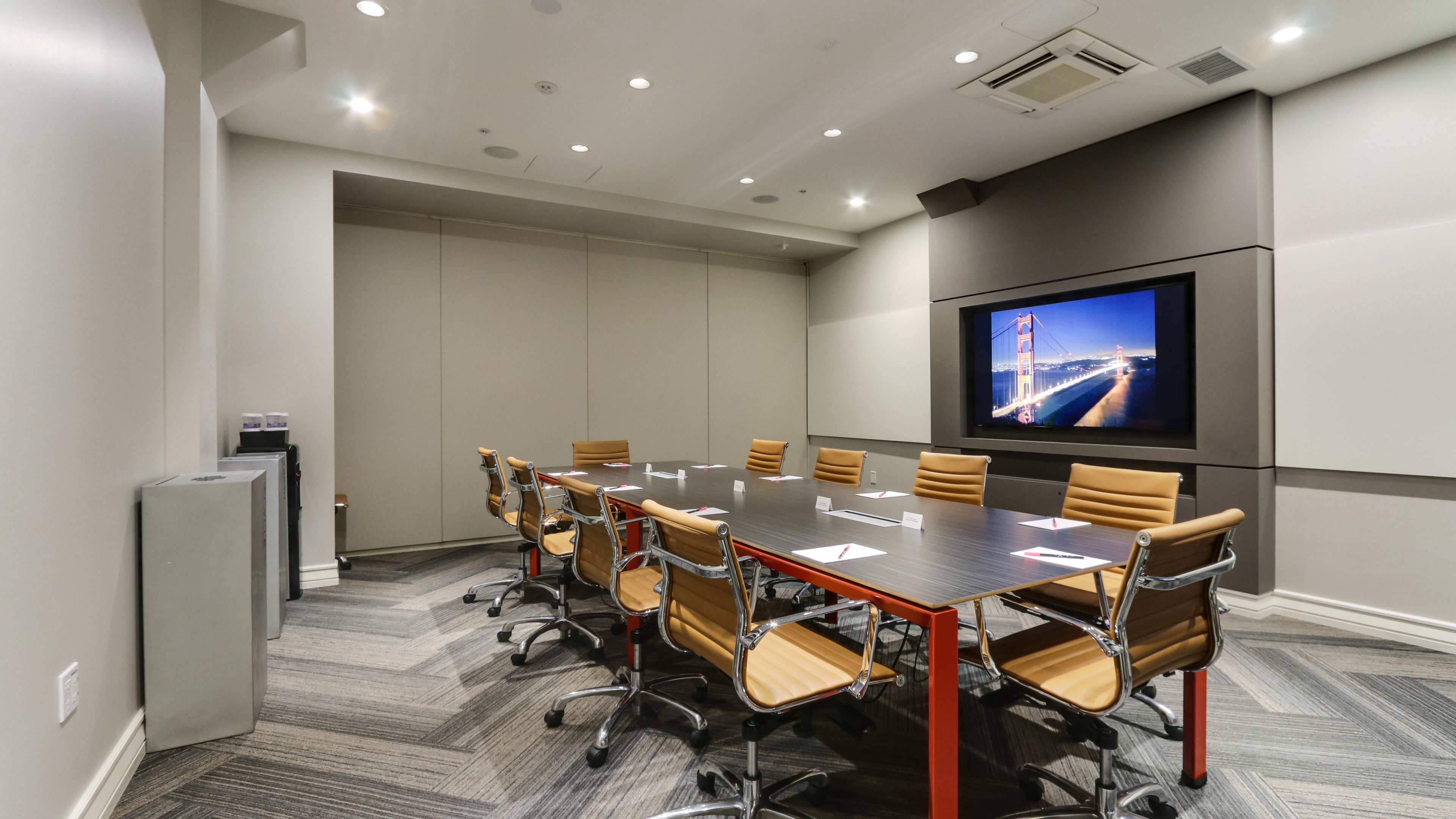 A modern conference room features a long table surrounded by eight chairs, with a large screen displaying an image on the wall.