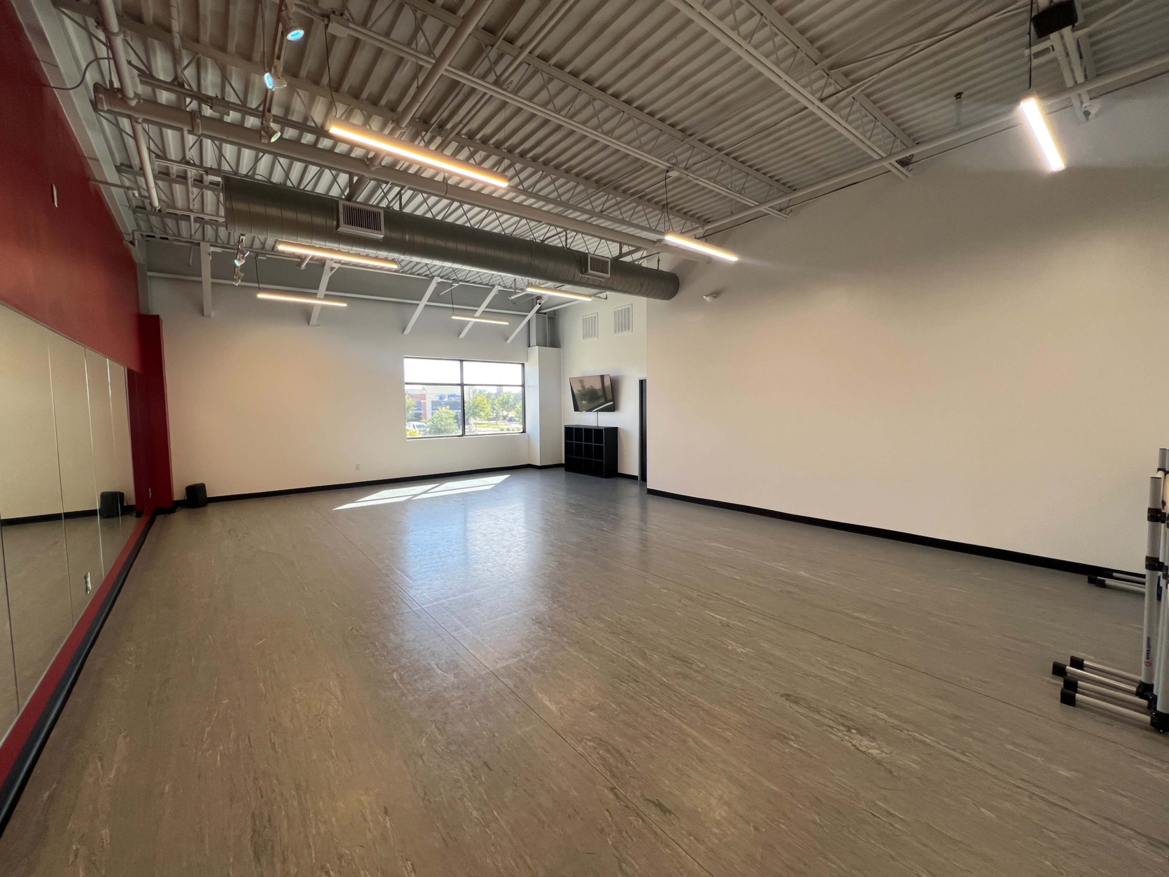 The image shows a spacious, empty fitness studio with large windows, a mirrored wall, and minimal equipment.