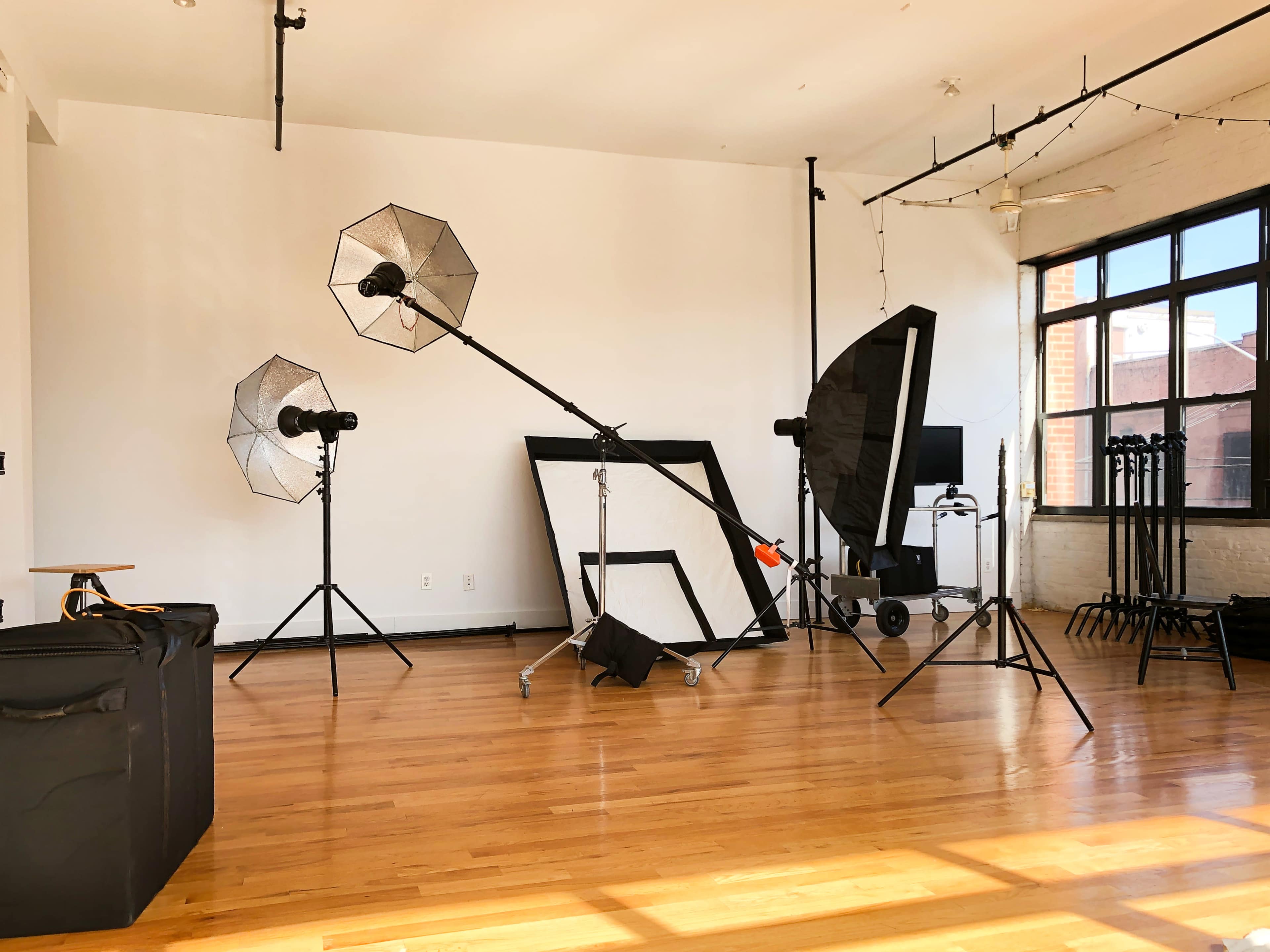 A photography studio setup featuring light stands, softboxes, and various backdrops arranged on a hardwood floor.