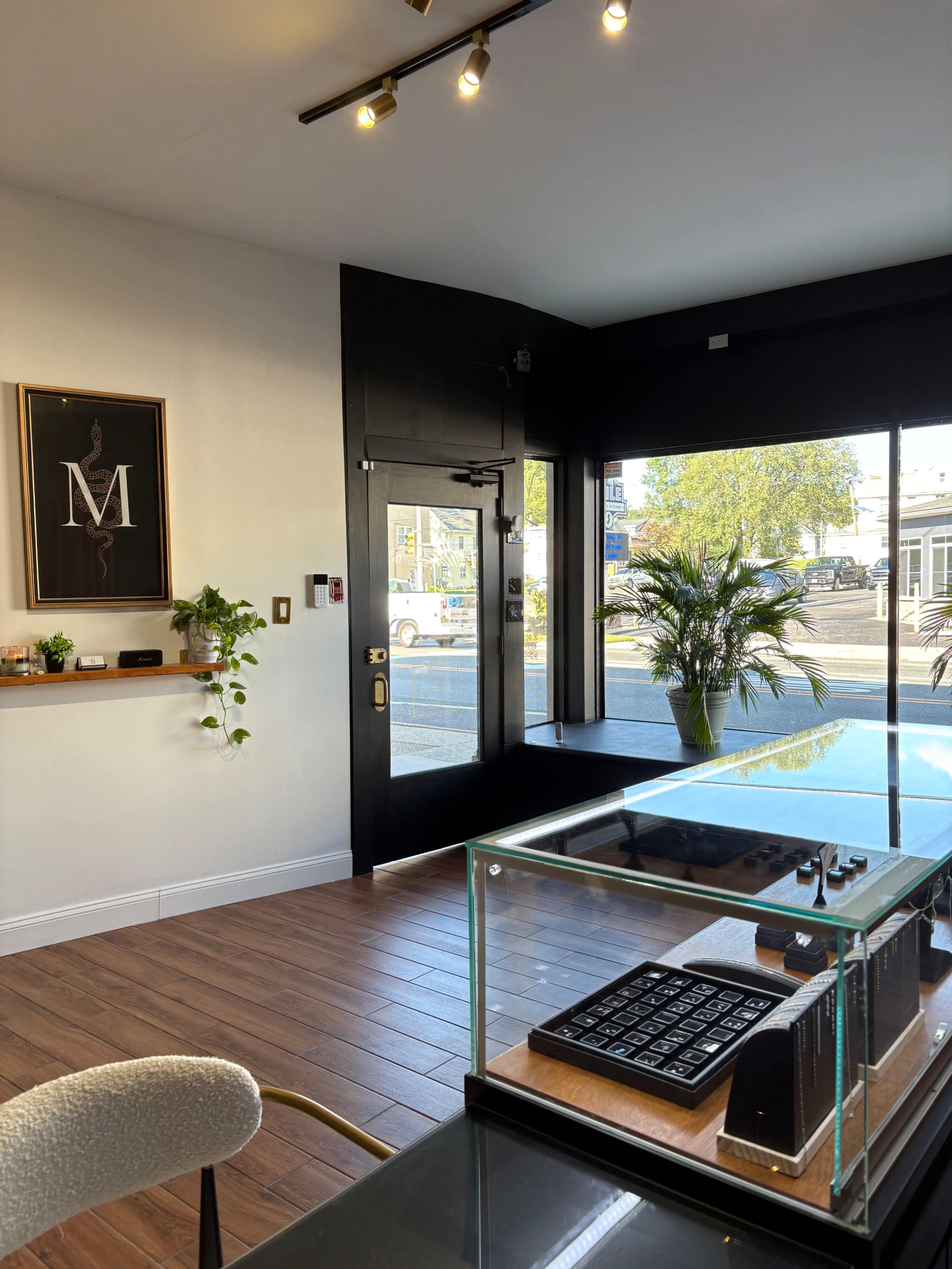 The image shows the interior of a modern storefront with large windows, a display table in the foreground, and a potted plant beside the entrance.