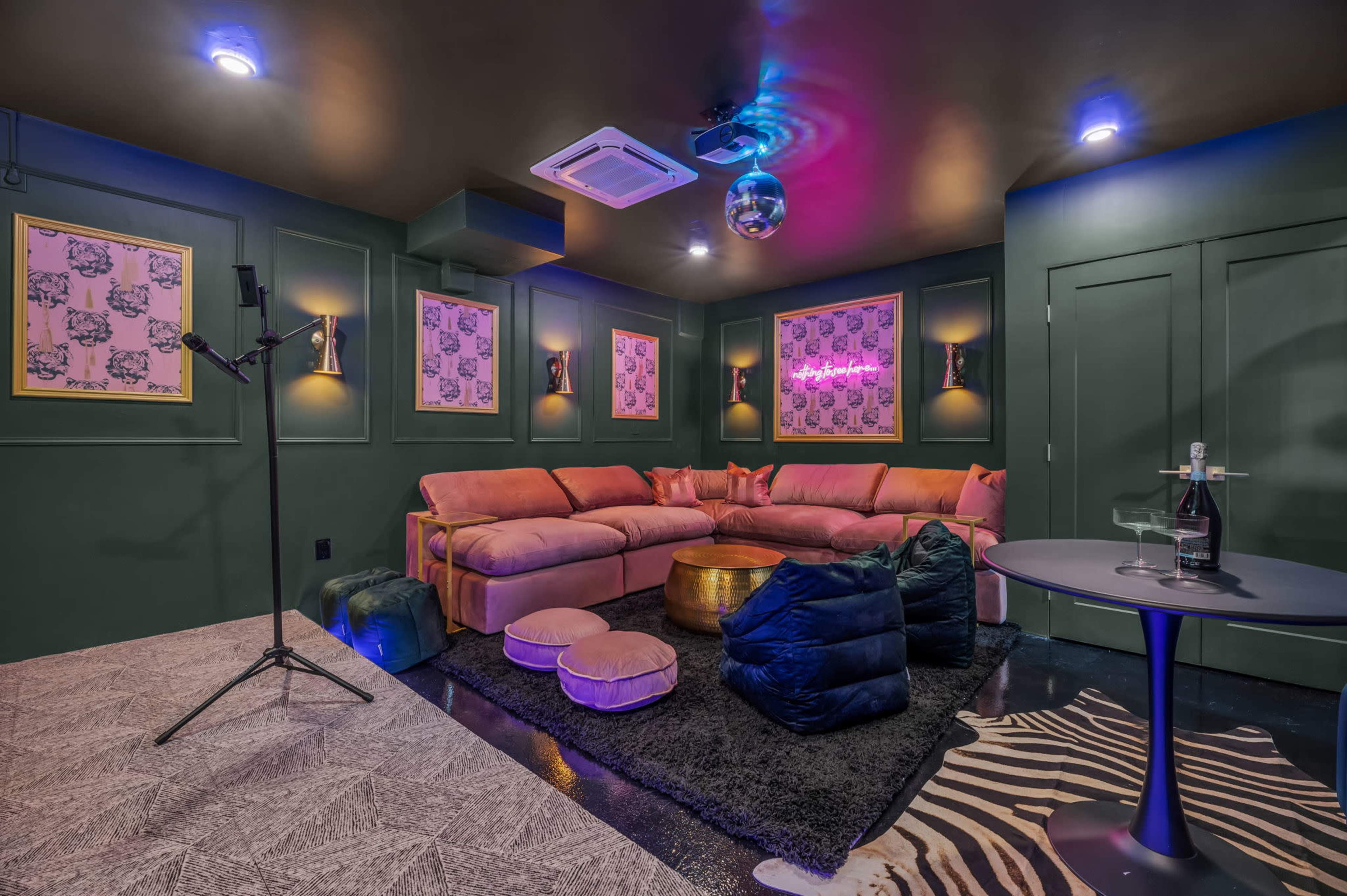 The image shows a stylish and cozy lounge area with a pink sectional sofa, decorative wall art, and a disco ball hanging from the ceiling.