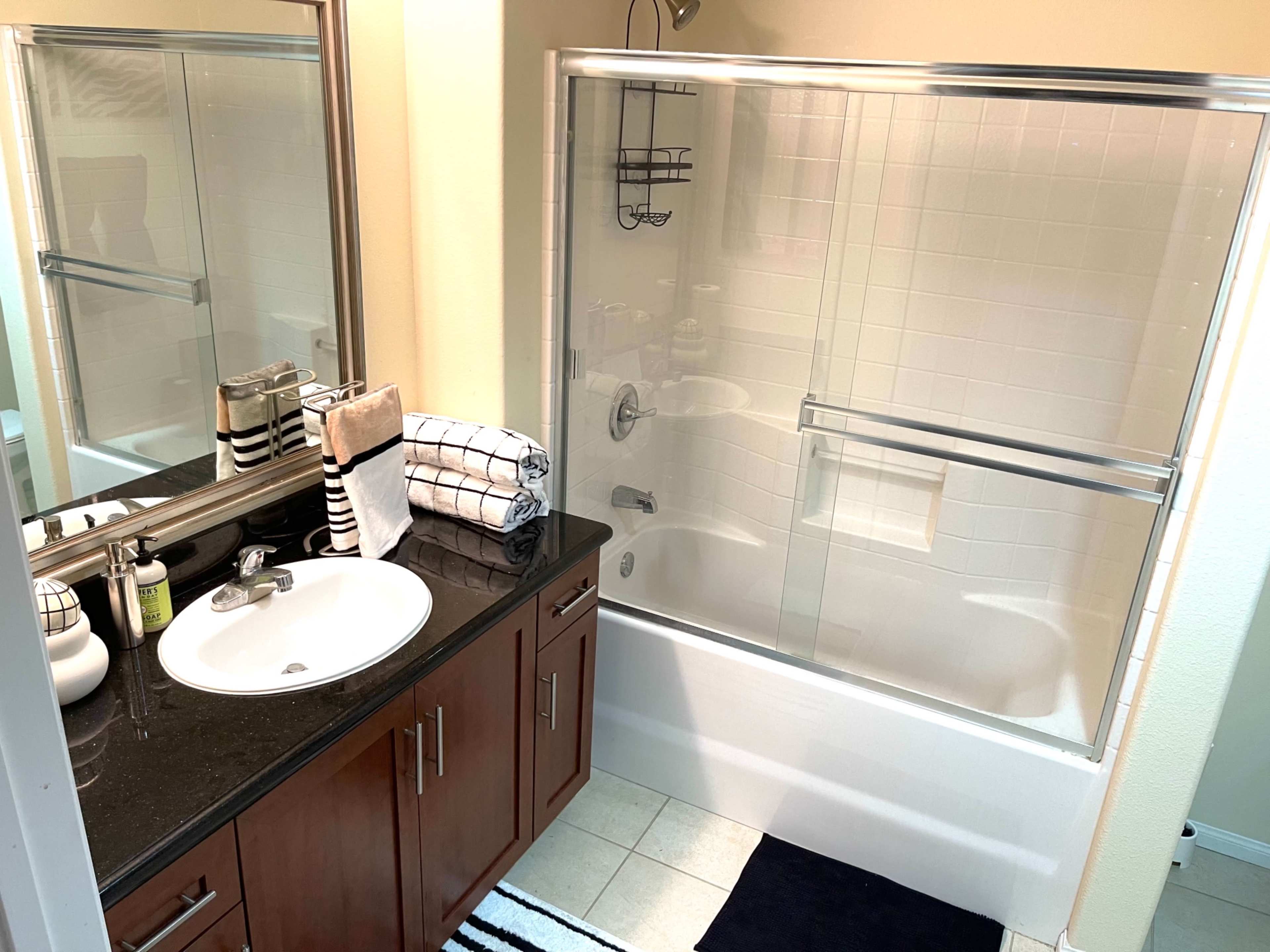 A bathroom with a glass-enclosed shower, a black granite countertop sink, and neatly arranged towels.