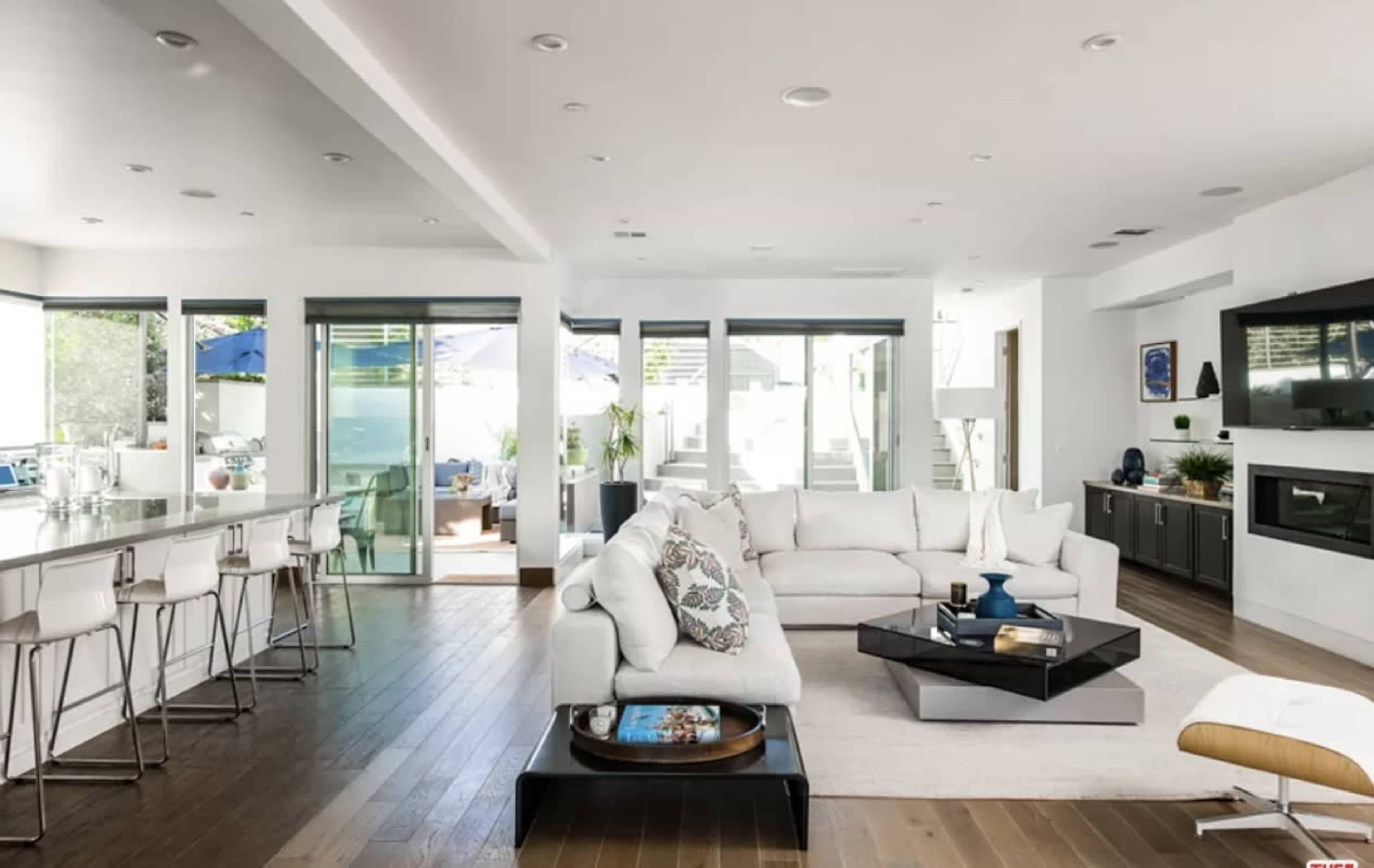 A modern living room with a white sofa, a coffee table, and a bar area leading to large glass doors that open to an outdoor space.
