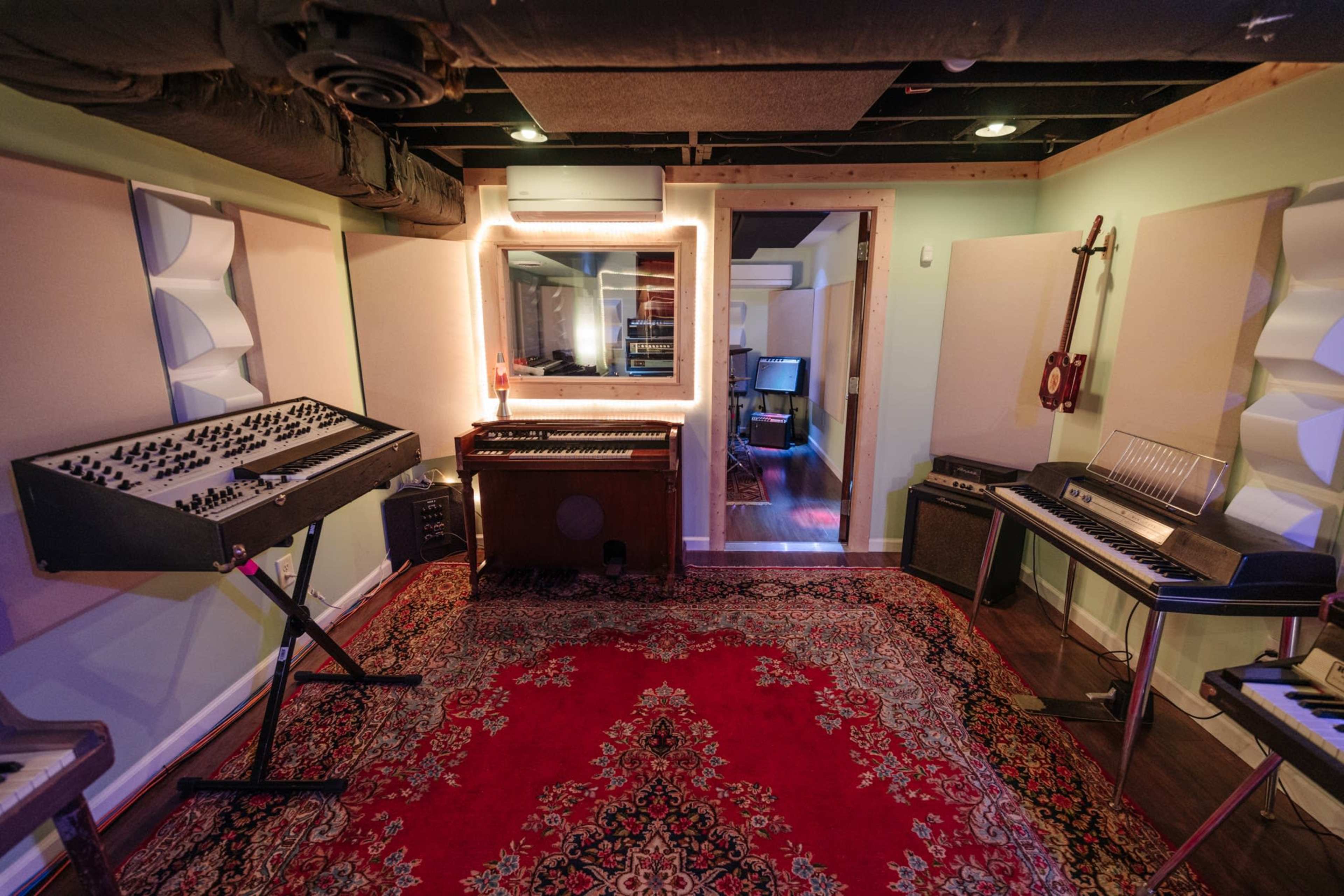 A music studio with various electronic instruments, including a synthesizer and keyboards, arranged around a patterned rug.