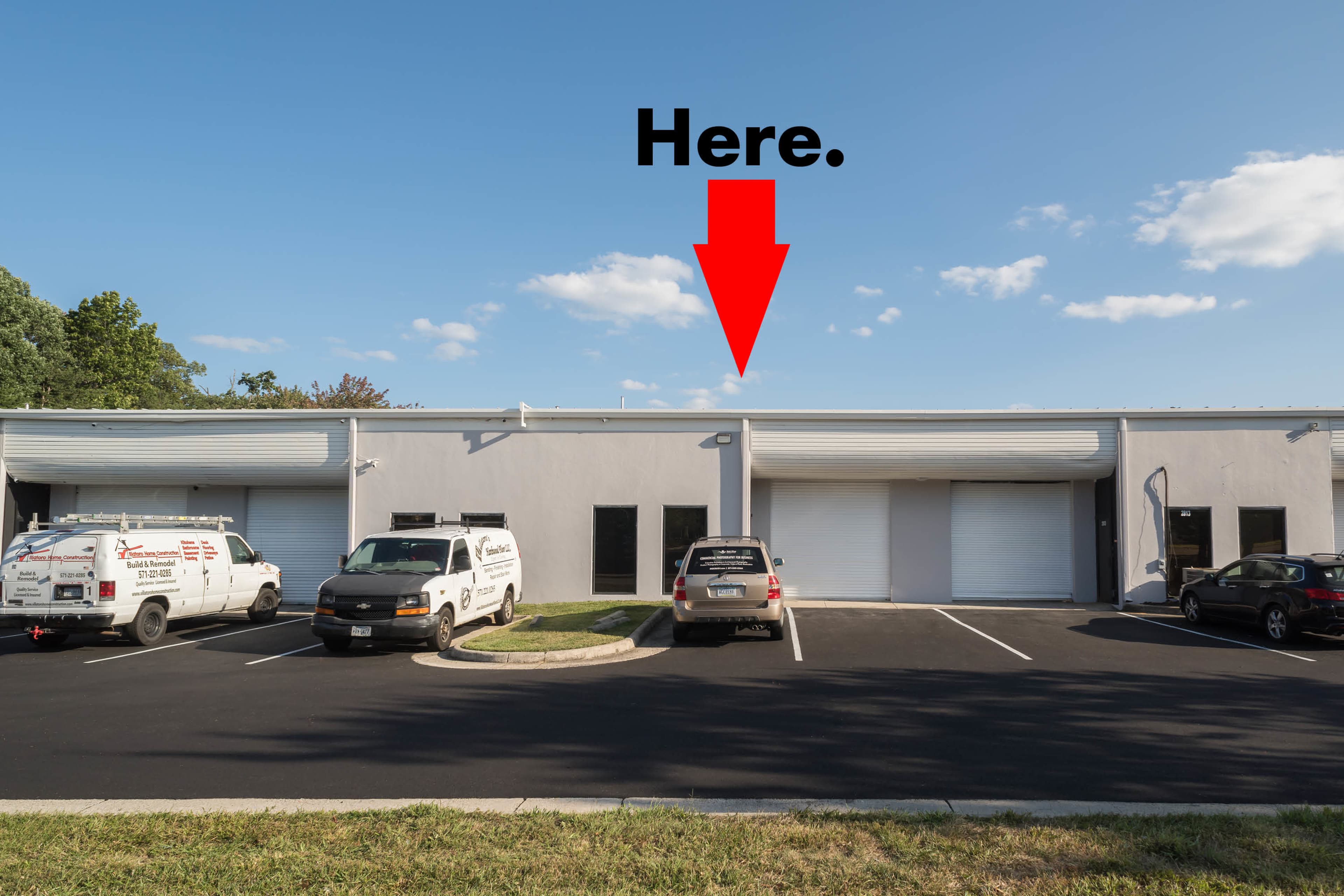 A row of commercial buildings with vehicles parked in front and a prominent arrow indicating a specific location.