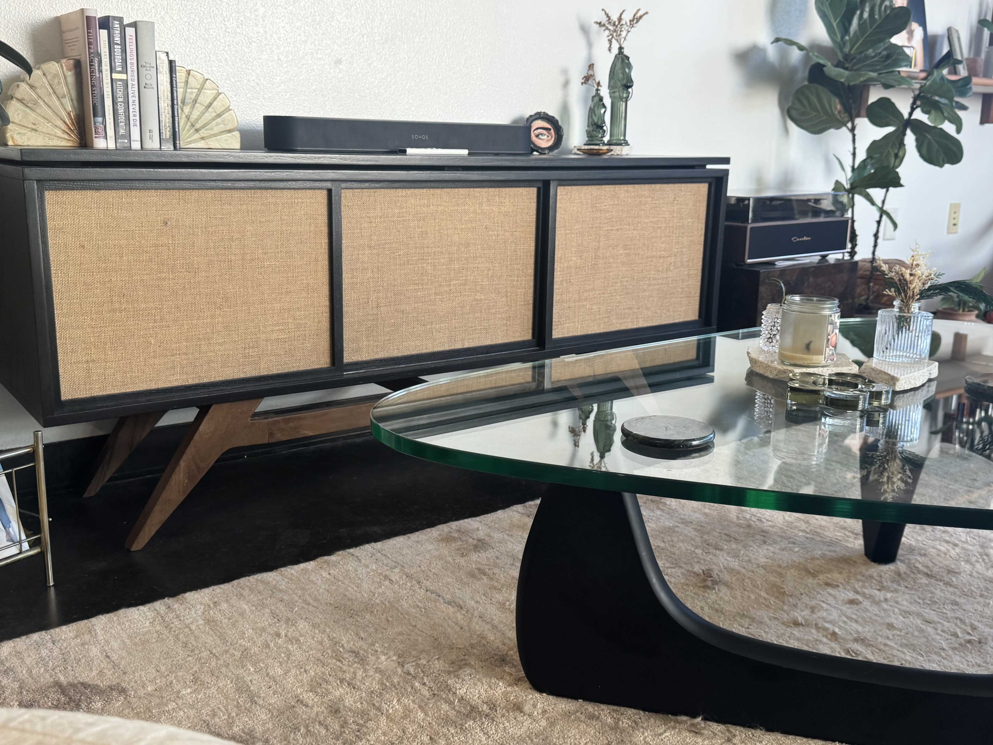 A mid-century modern cabinet with woven doors is positioned against a wall, alongside a glass coffee table and decorative items on a rug.