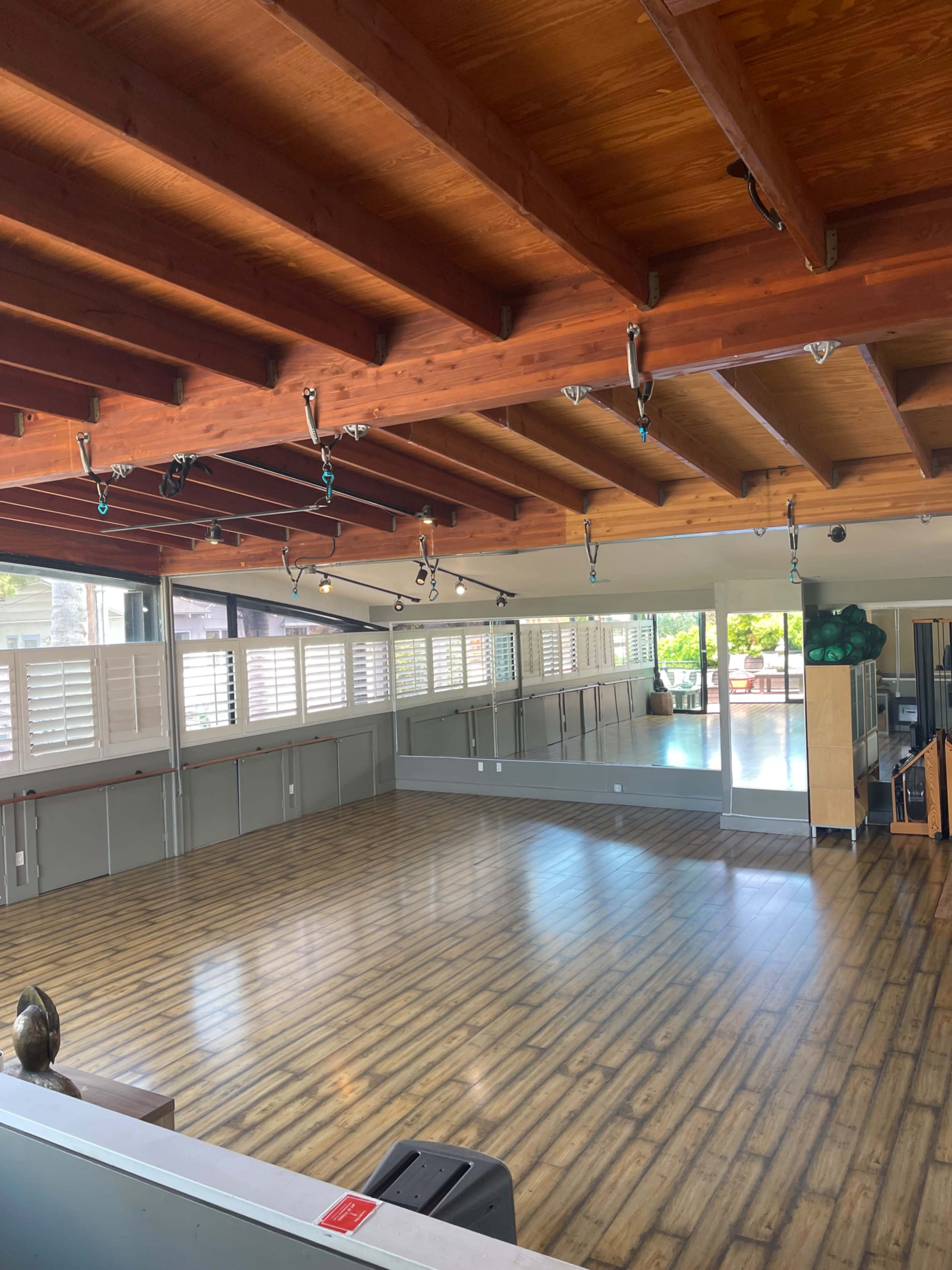 A spacious studio with wooden flooring, large mirrors, and natural light coming through windows.