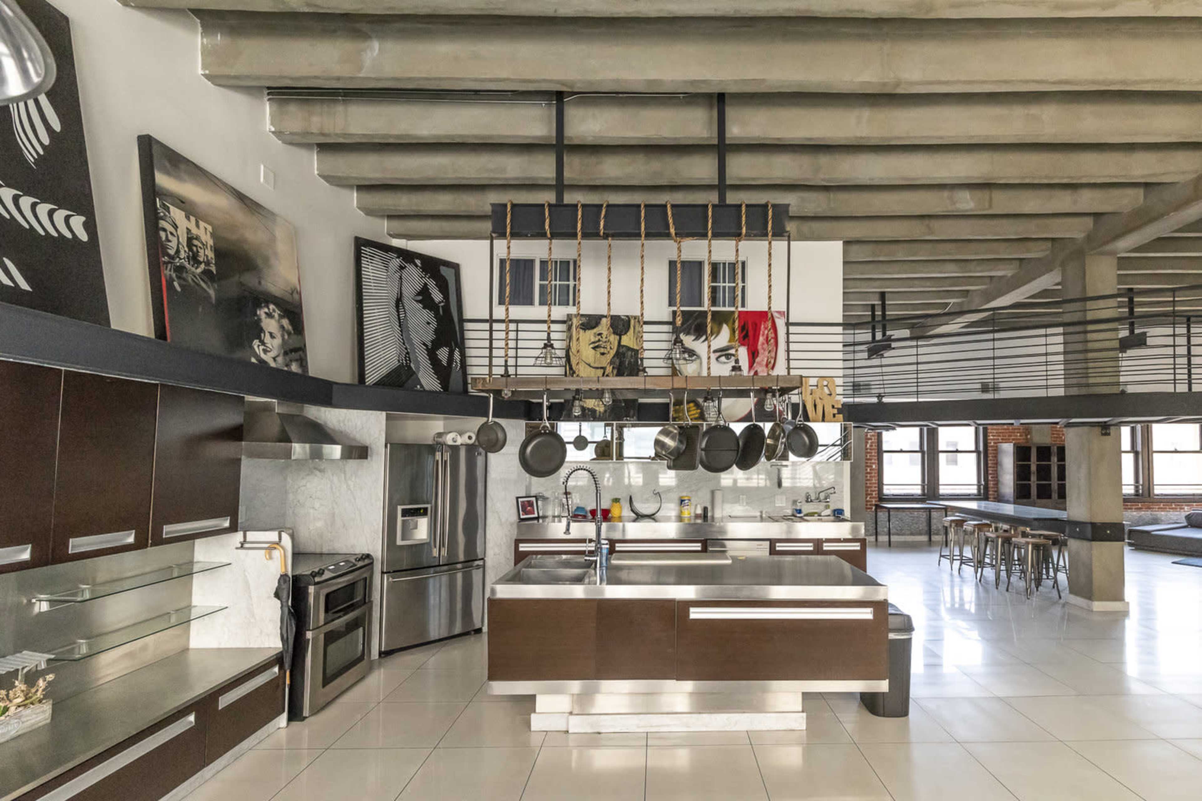 A modern kitchen with a central island, sleek cabinetry, and industrial-style decor featuring exposed beams and large artwork on the walls.