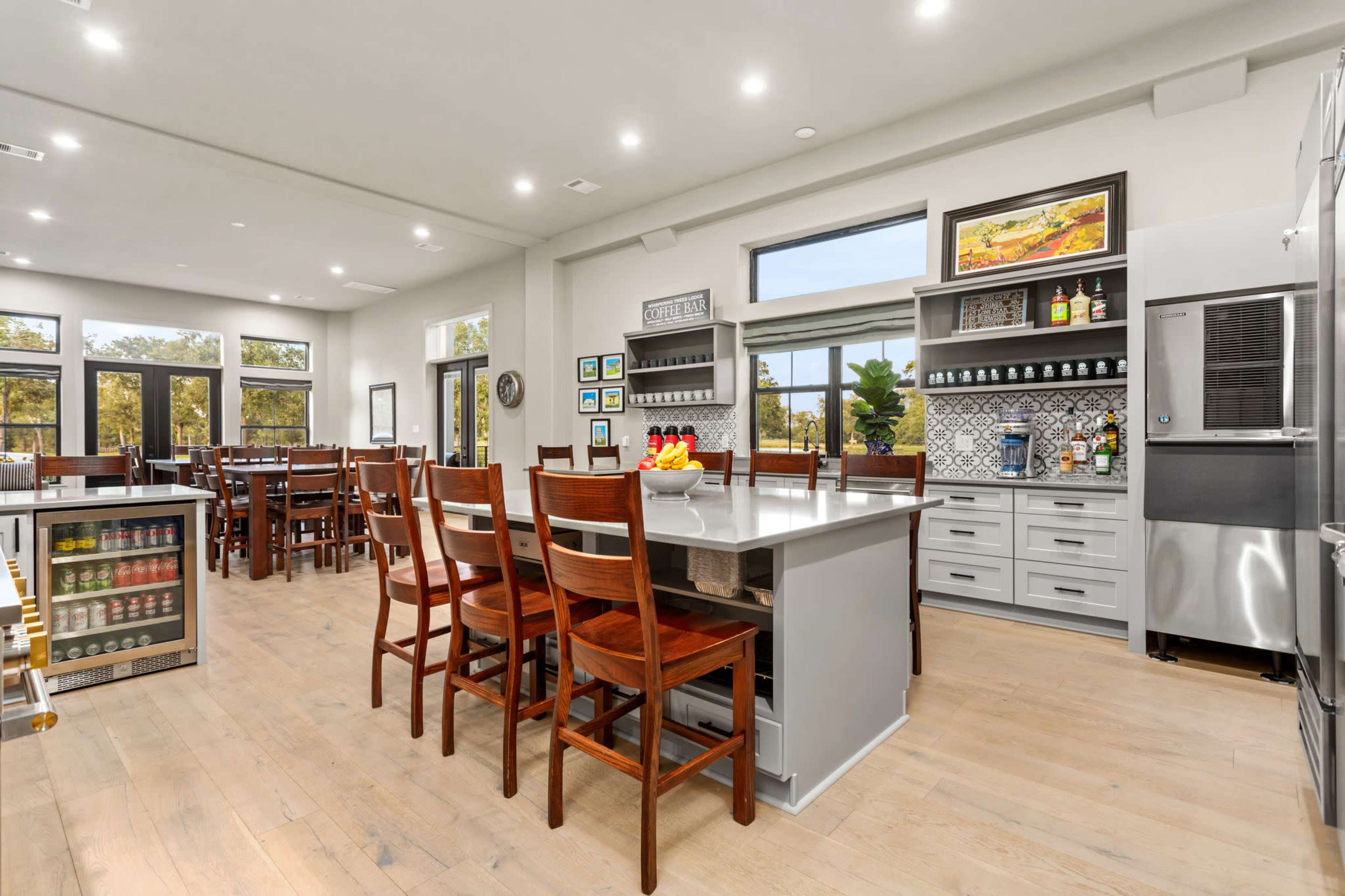 A modern kitchen with a central island, wooden stools, and large windows overlooking a wooded area.