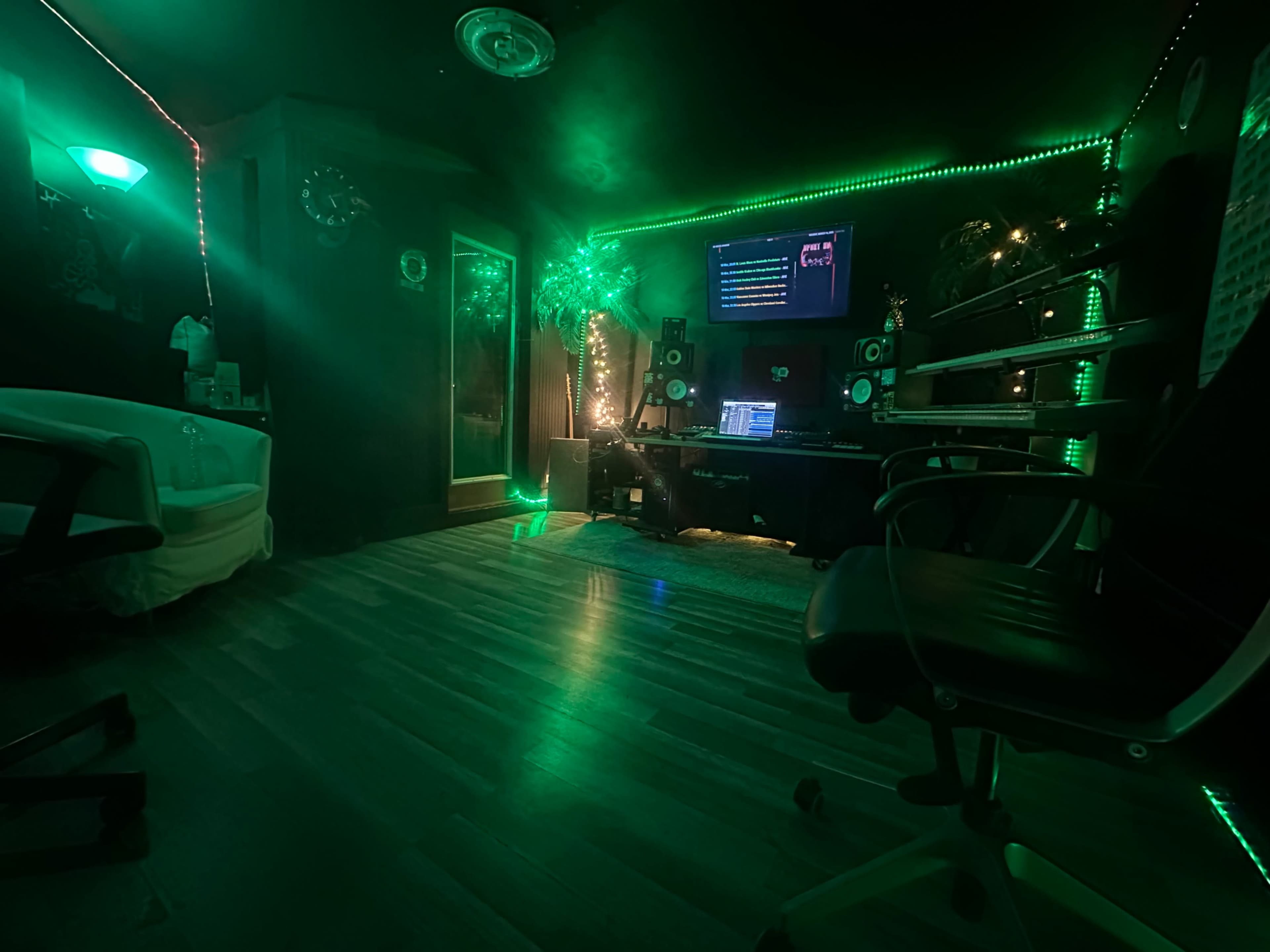 The image shows a music studio with green LED lights, a computer setup, and sound equipment on a wooden floor.