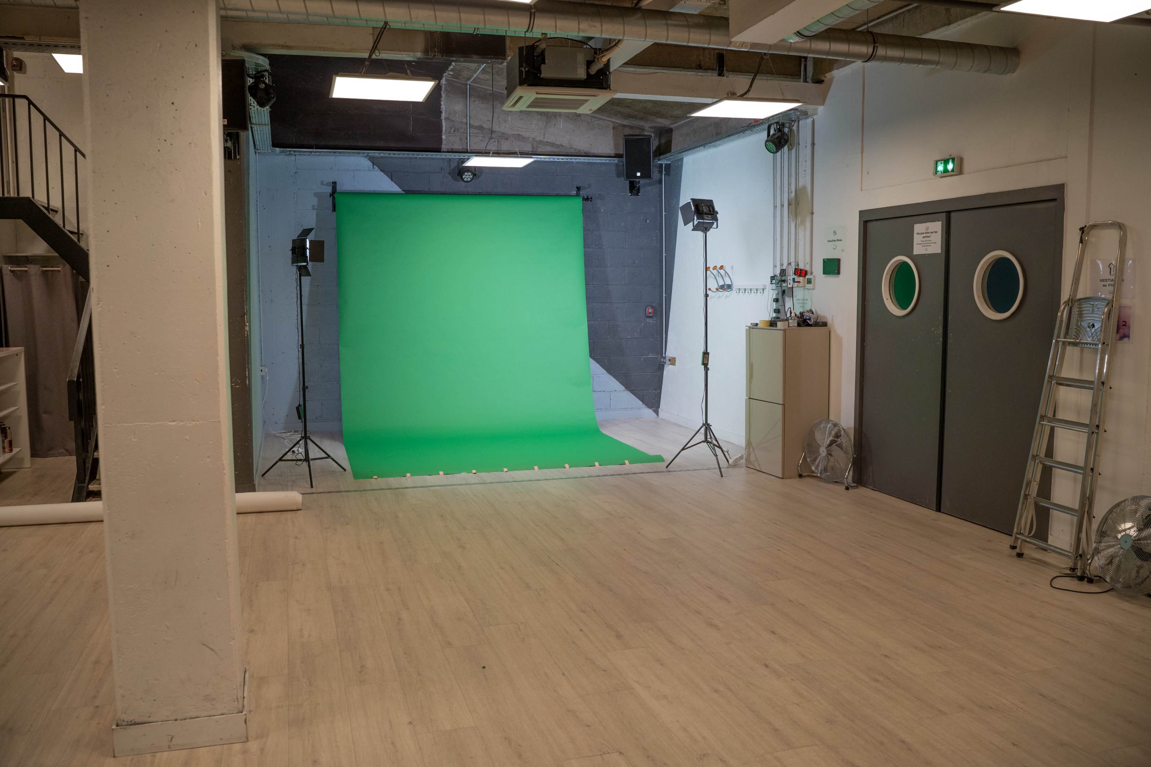 A studio space with a green backdrop and two lights set up for photography or video production.