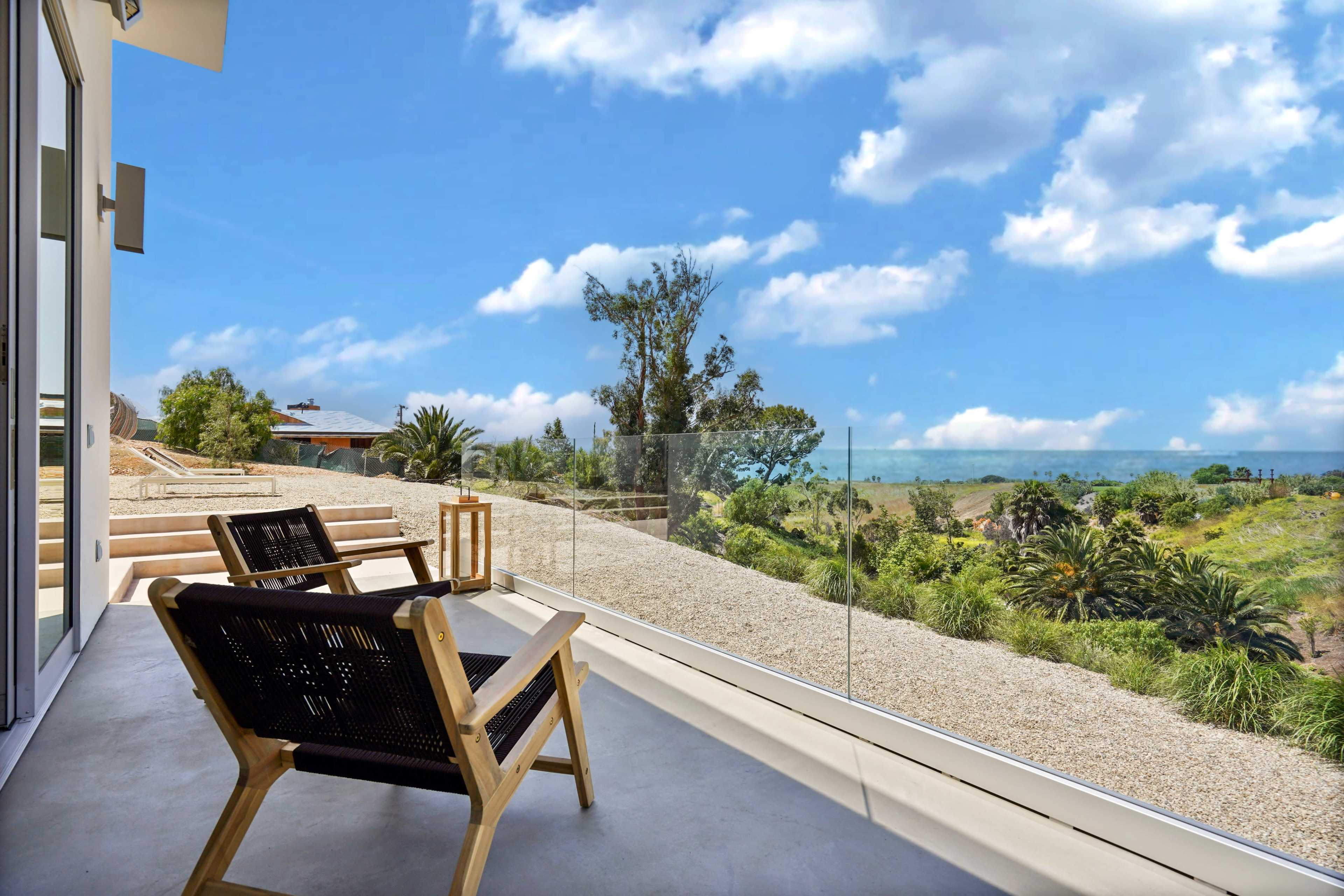 A patio with two wooden chairs facing a landscape of greenery and blue skies.
