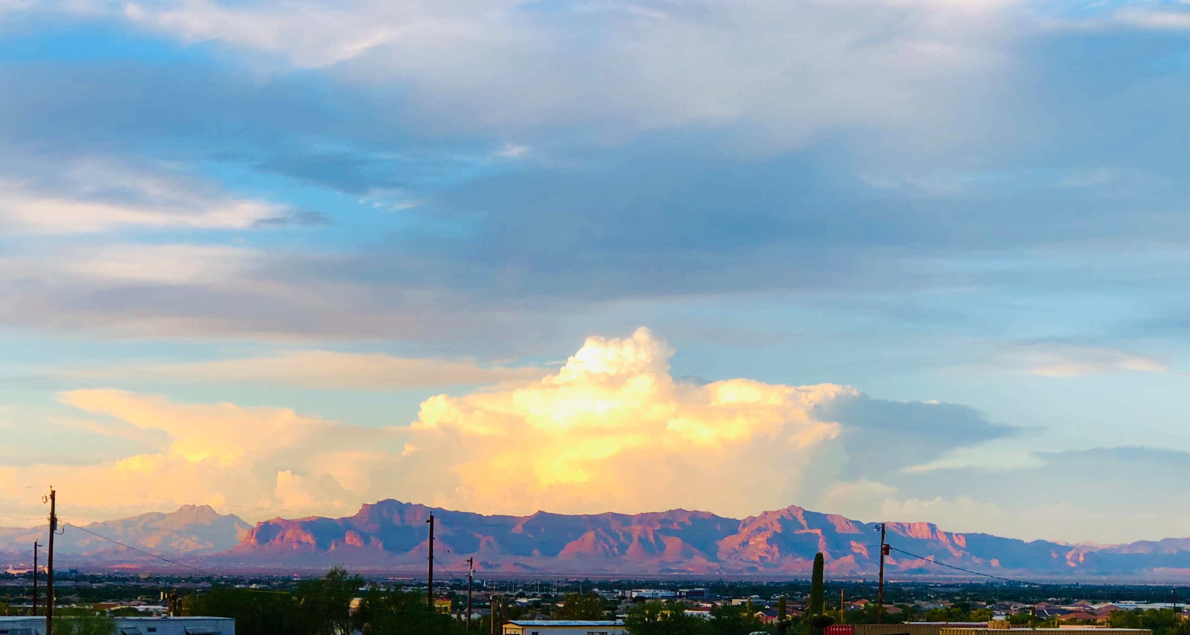 A sprawling view of mountains under a blue sky with scattered clouds and a colorful sunset.