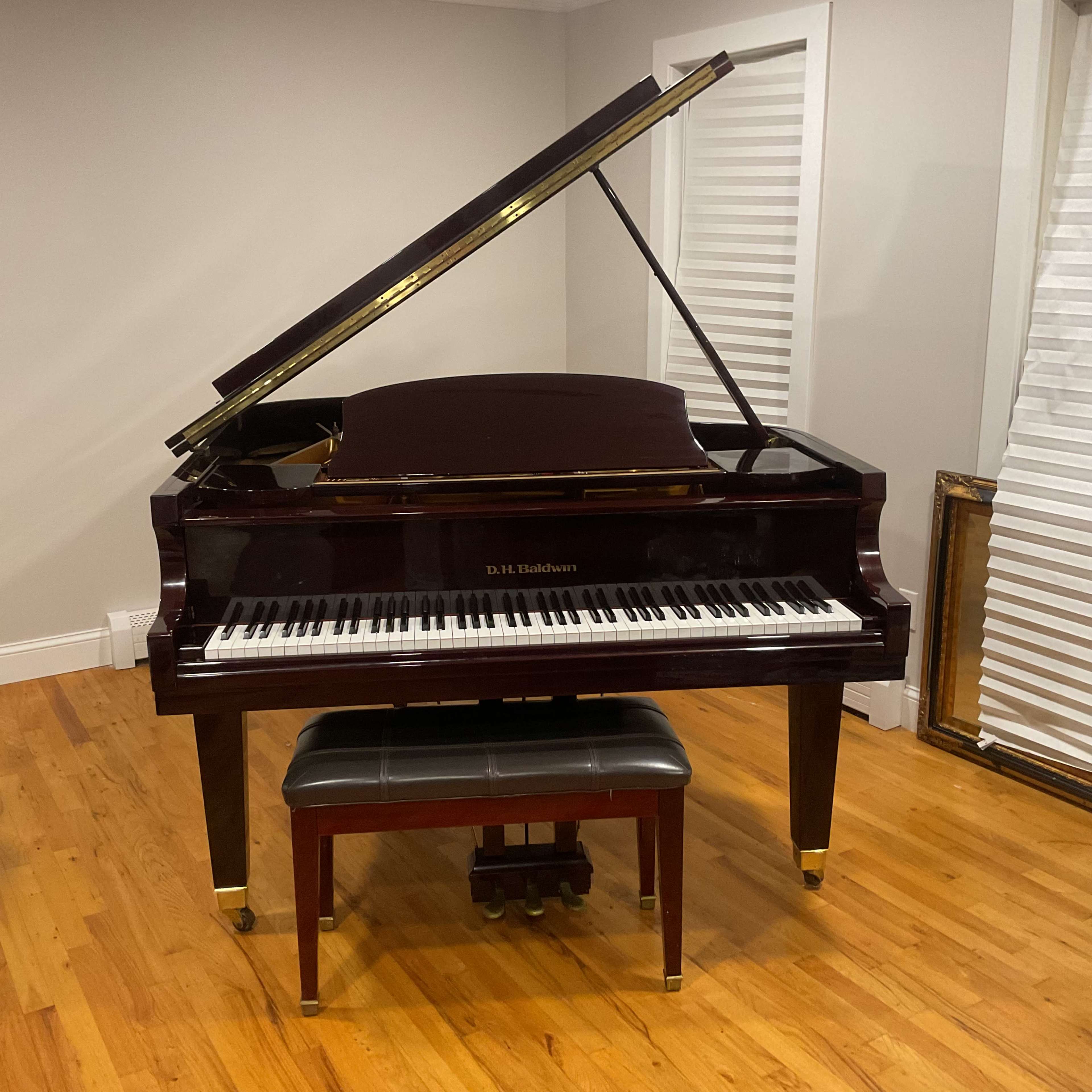 A polished grand piano with the lid open is positioned in a room with hardwood flooring and light-colored walls.