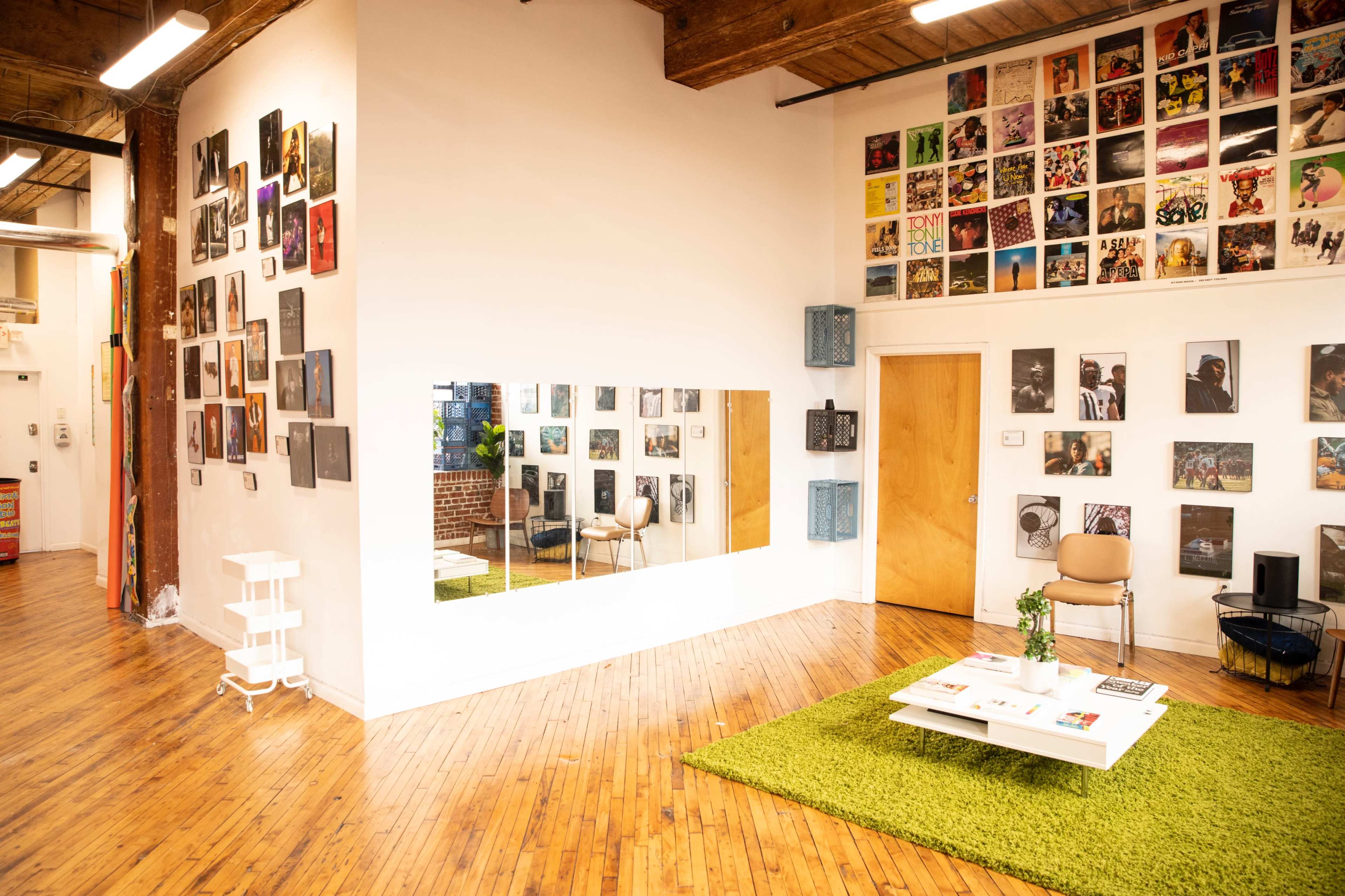 A bright, open space with wooden floors, adorned with various framed photographs on the walls, a green rug on the floor, and a coffee table surrounded by a chair.