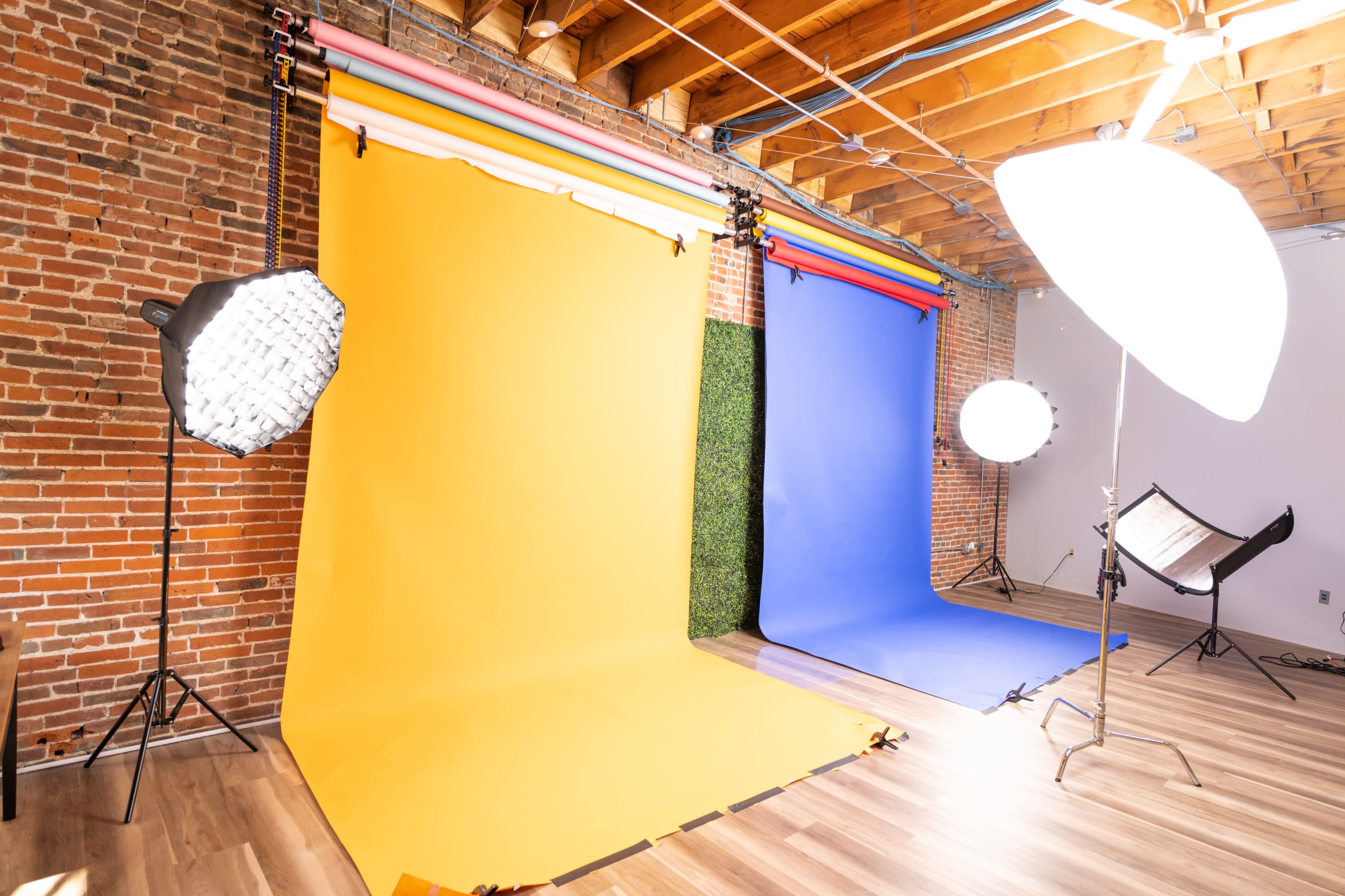 The image shows a photography studio with yellow, blue, and green backdrops, along with lighting equipment set up for a photo shoot.