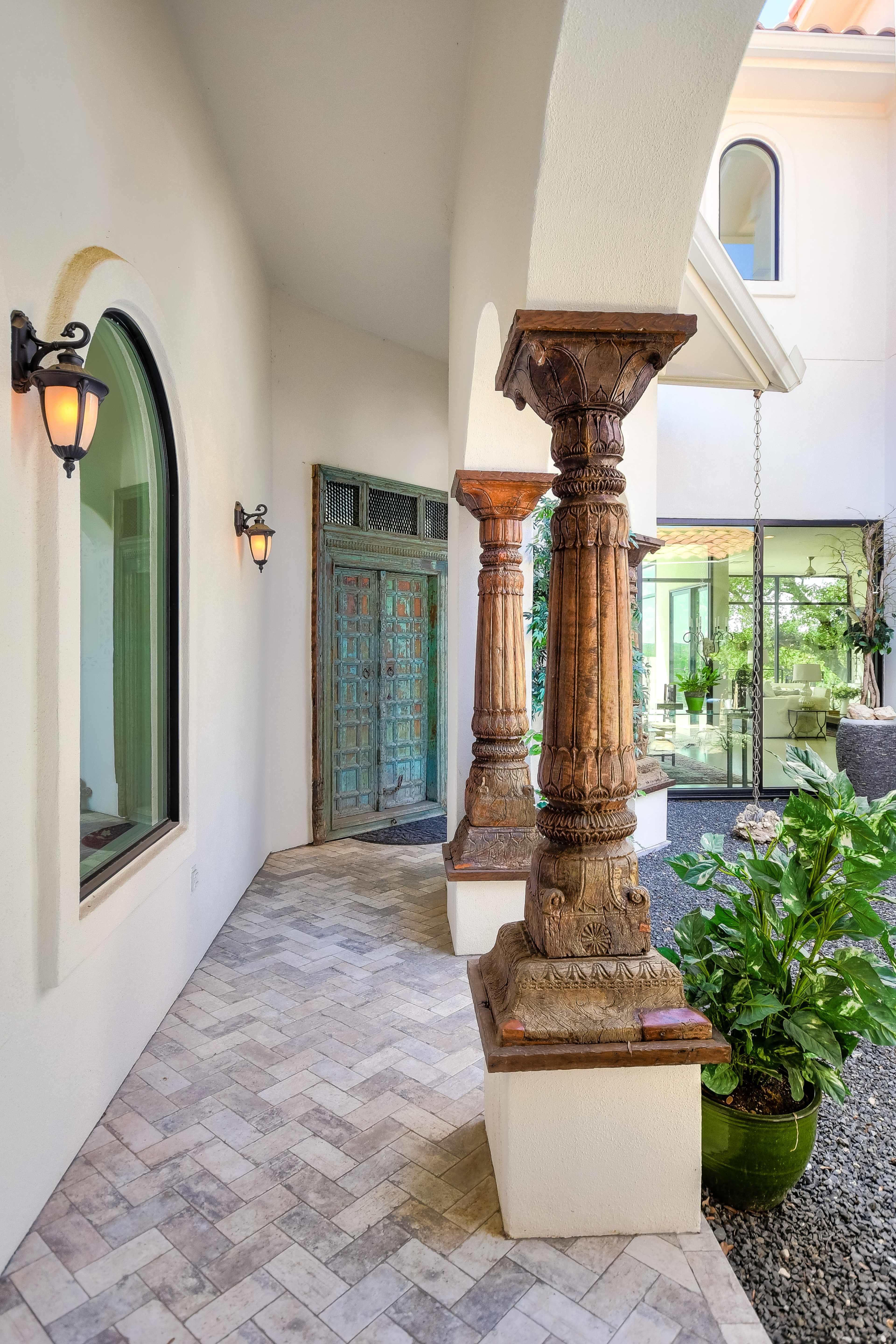 A courtyard entrance with arched doorways, decorative columns, and a stone pathway alongside potted plants.