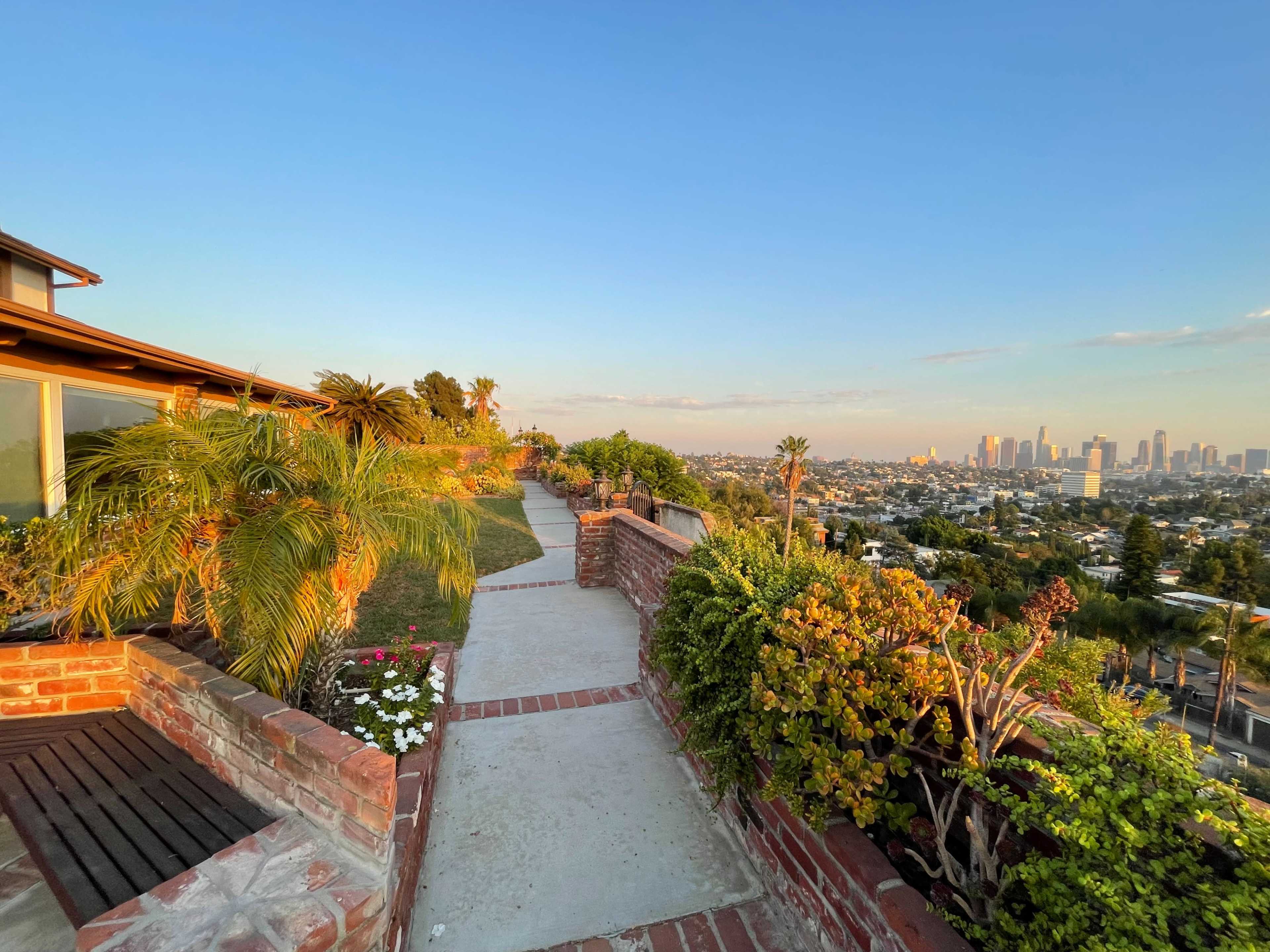 A paved path winds through landscaped greenery, leading towards a view of the city skyline in the distance.
