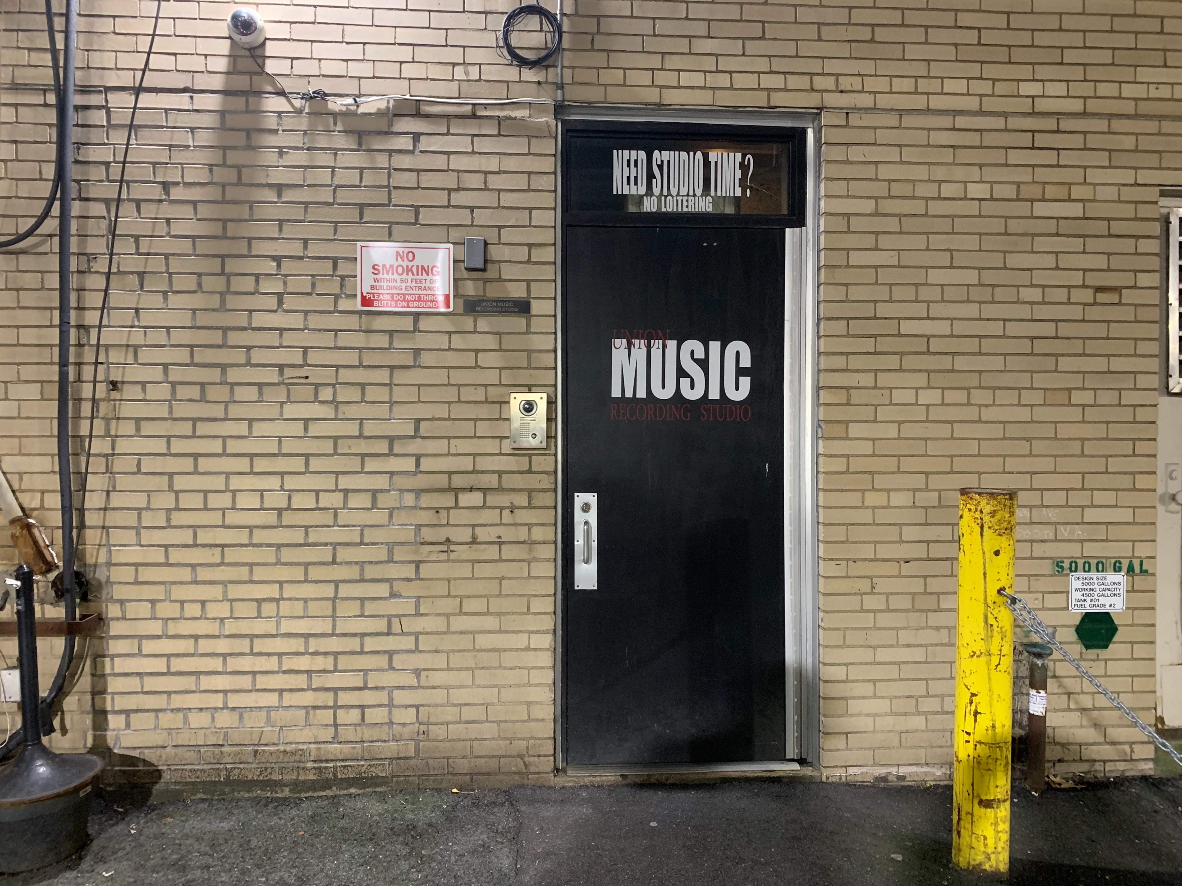 A black door marked "MUSIC" leads to a recording studio, with a no smoking sign and a yellow post nearby.