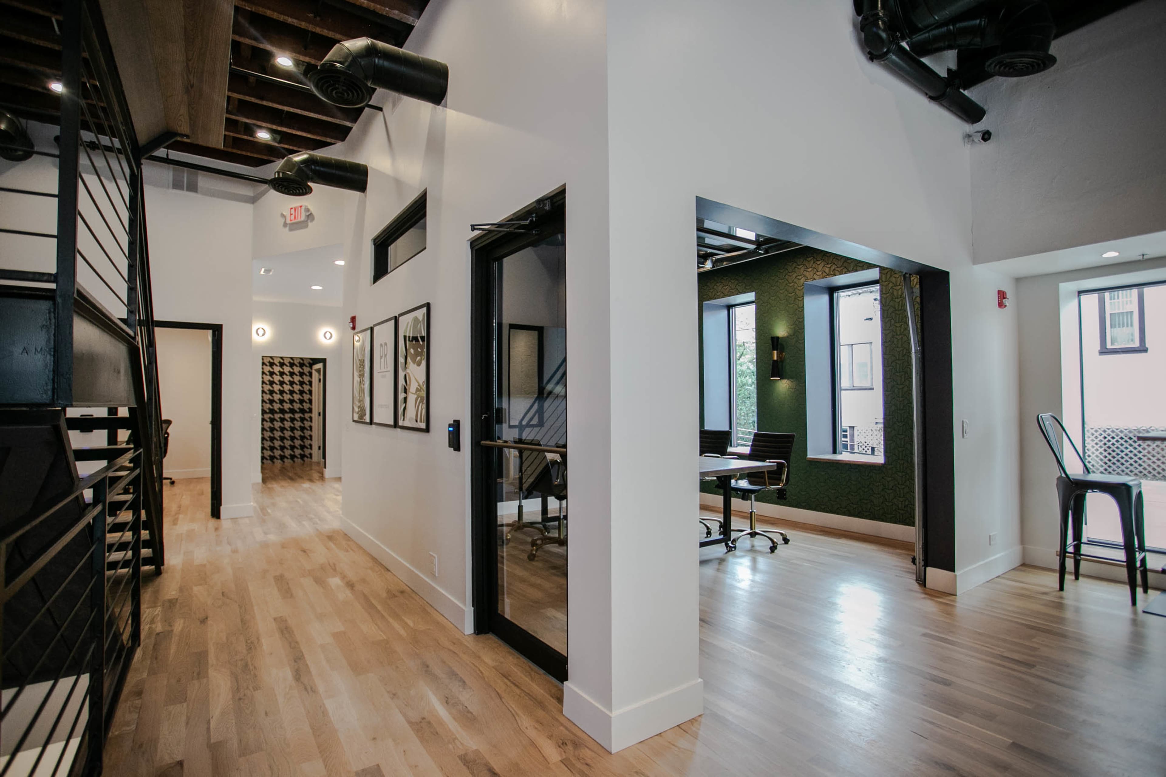 The image shows a modern interior with wooden floors, exposed beams, and an open layout featuring a hallway, a meeting area with large windows, and a staircase.