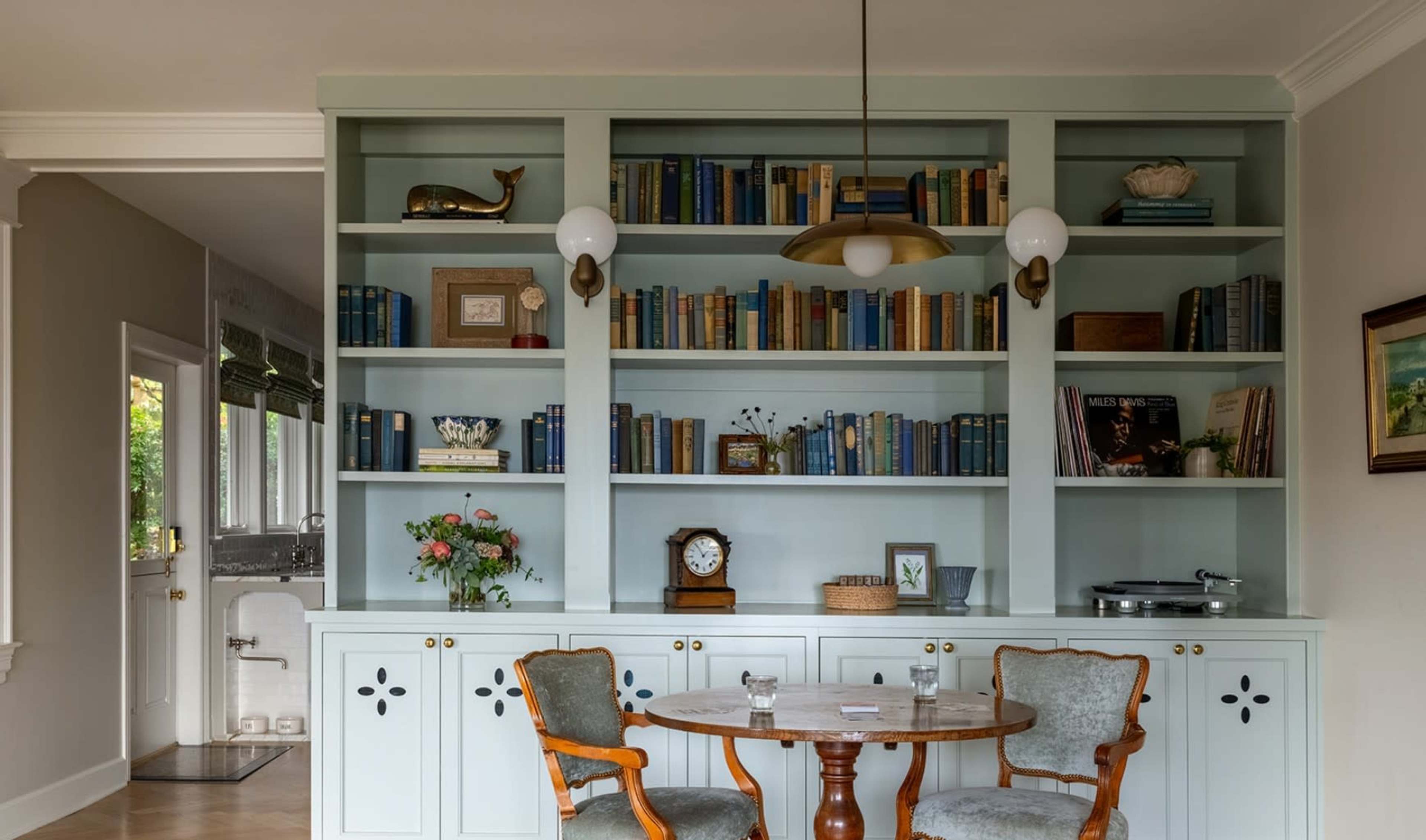 A cozy dining area features a wooden table with two chairs in front of a built-in bookshelf filled with books, decorative items, and a vintage record player.