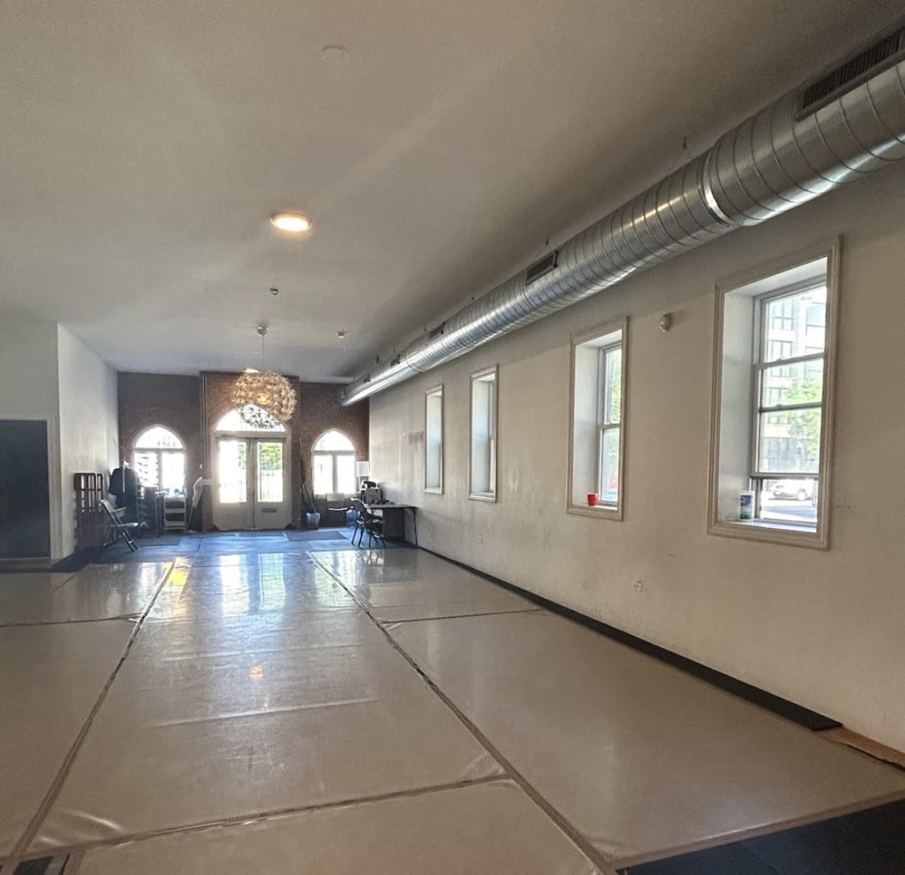 The image shows an empty indoor space with padded flooring, large windows, and a door leading to the outside.