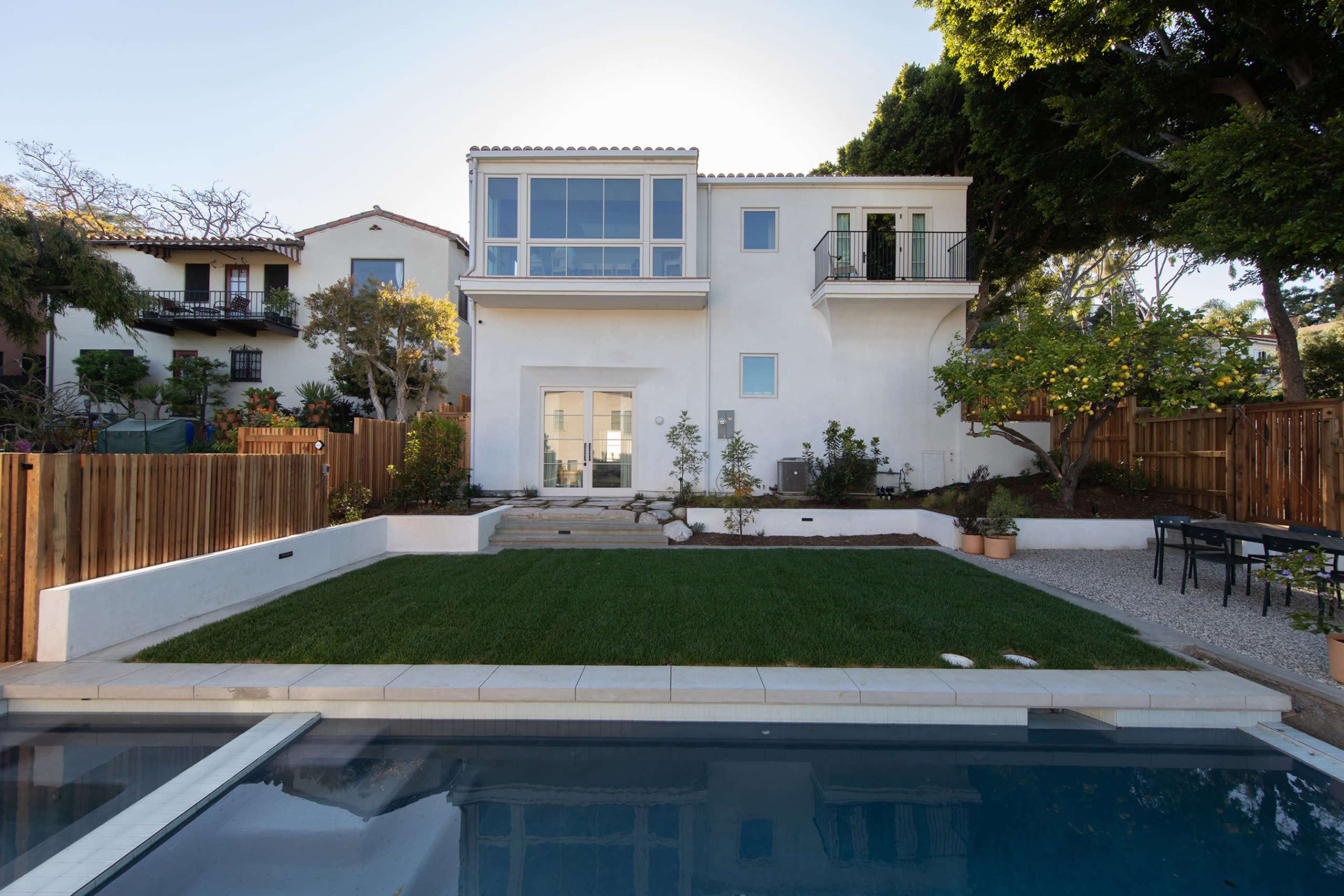 A modern two-story house with large windows and a backyard featuring a lawn, patio, and swimming pool.