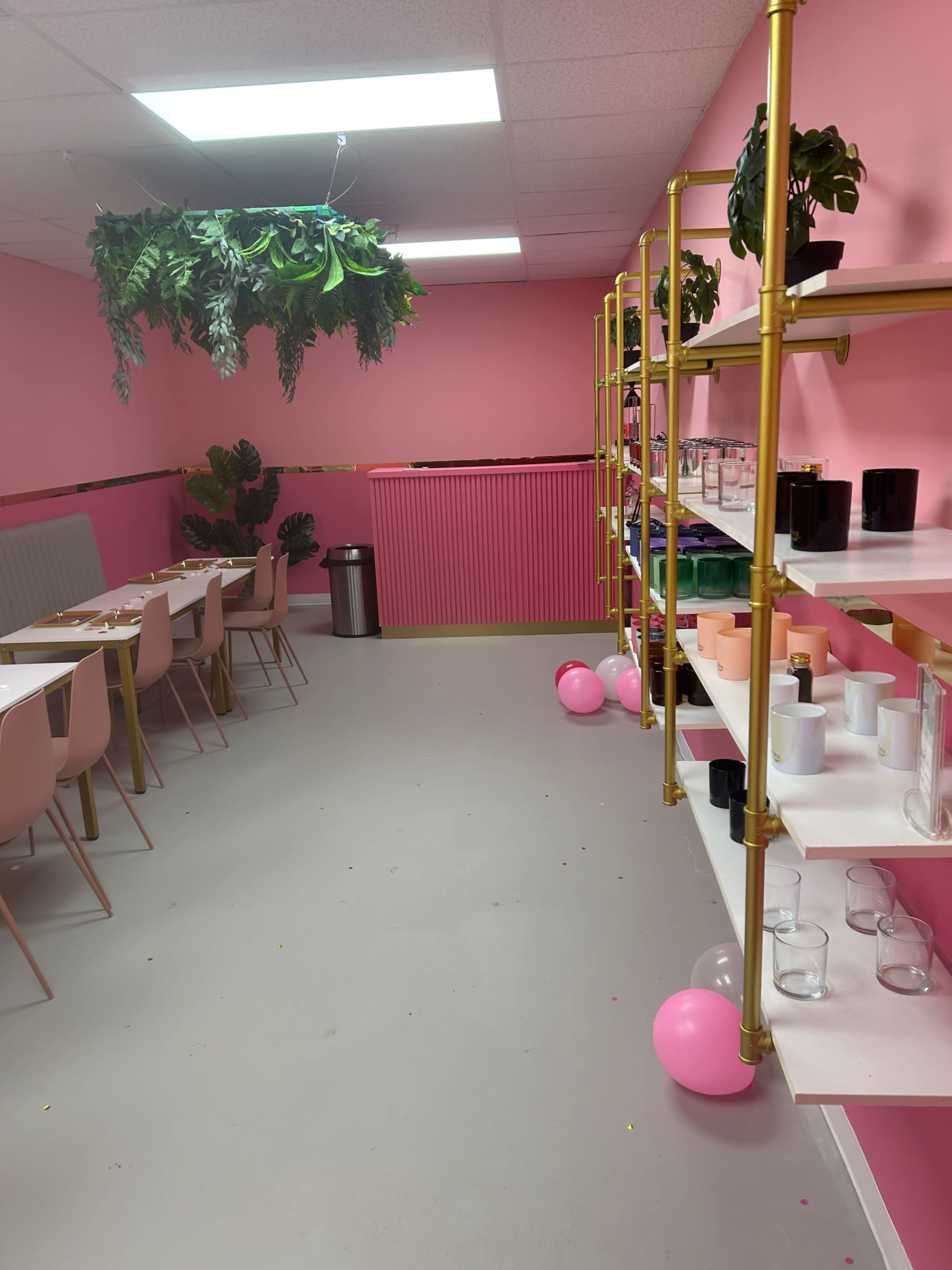The image shows a brightly colored room with pink walls, a long table with chairs, and shelves displaying various glassware and decorative items.