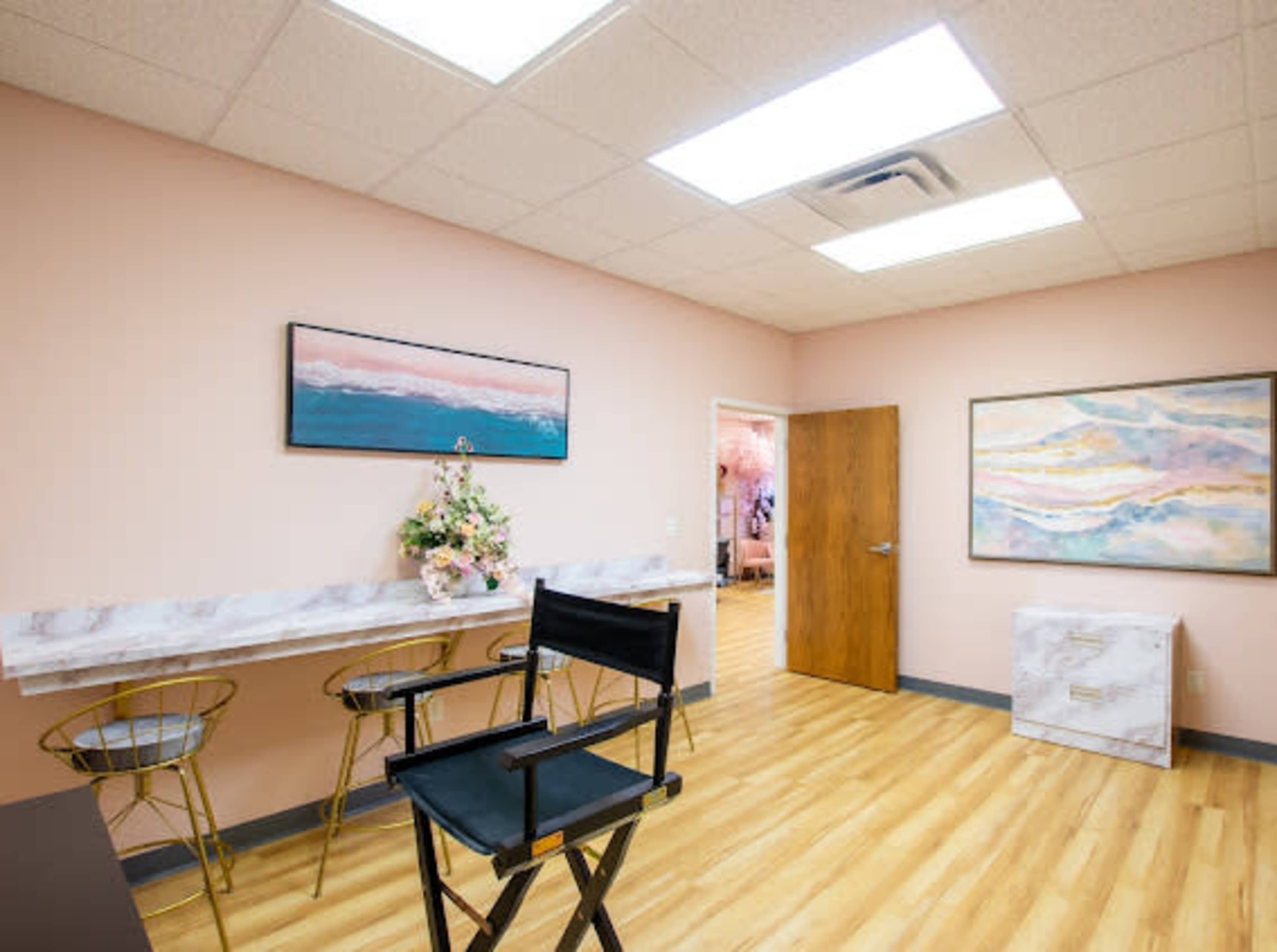 A well-lit room with light pink walls, a marble-topped table, a director's chair, and two colorful paintings on the walls.