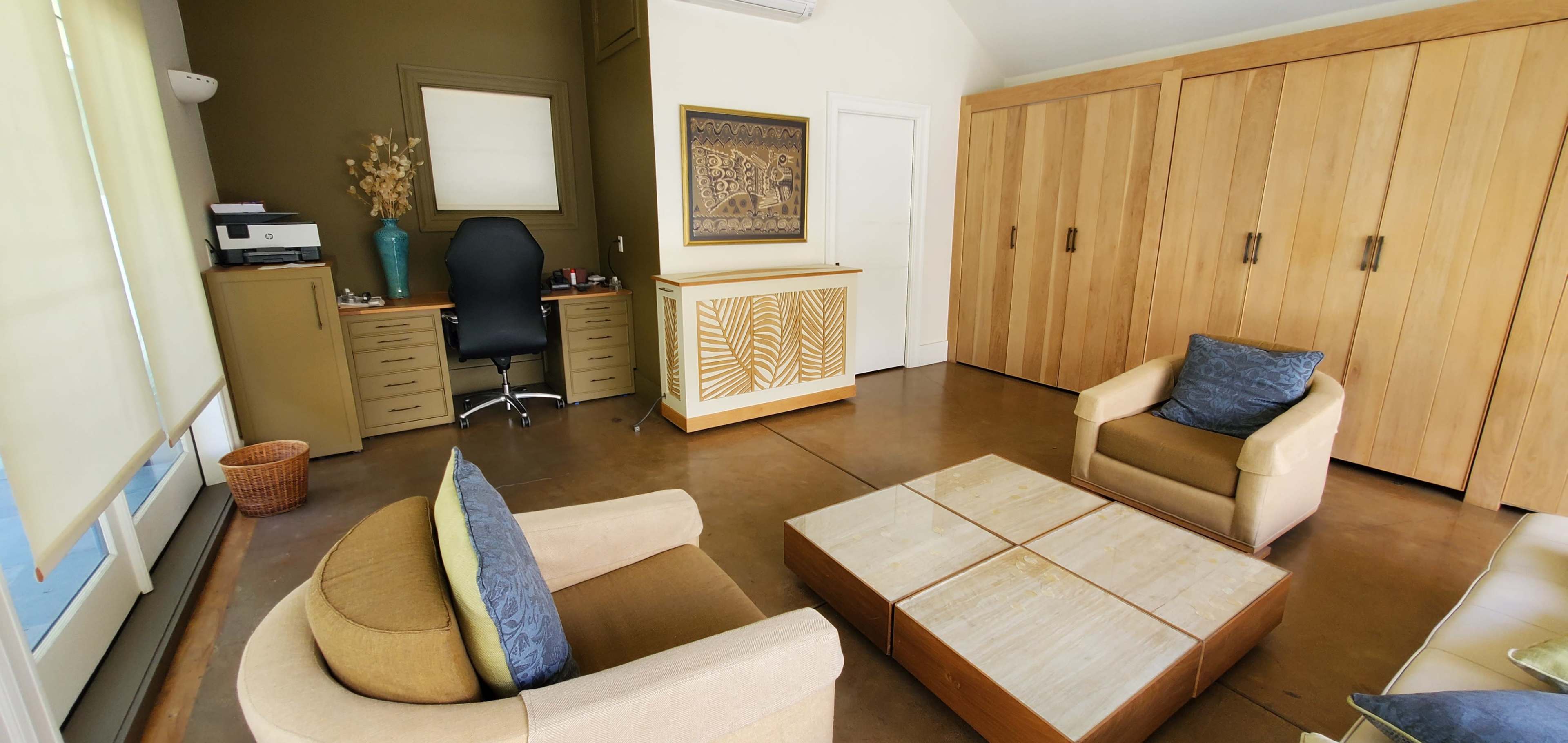 A small office space featuring a desk with a chair, a set of wooden storage cabinets, two armchairs with cushions, and a coffee table in the center.