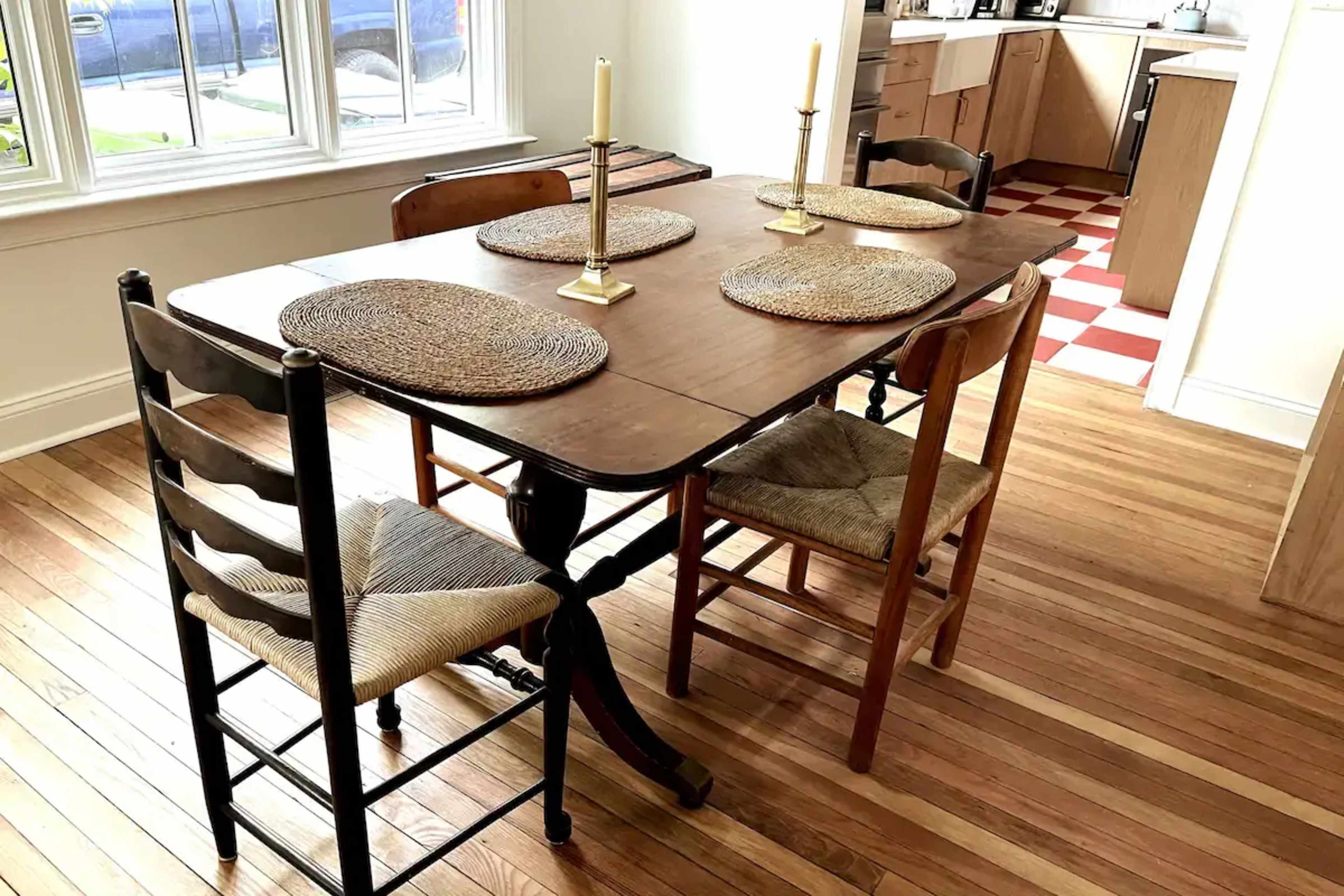 A wooden dining table set with four chairs and two candlesticks, placed in a kitchen with a checkered floor.