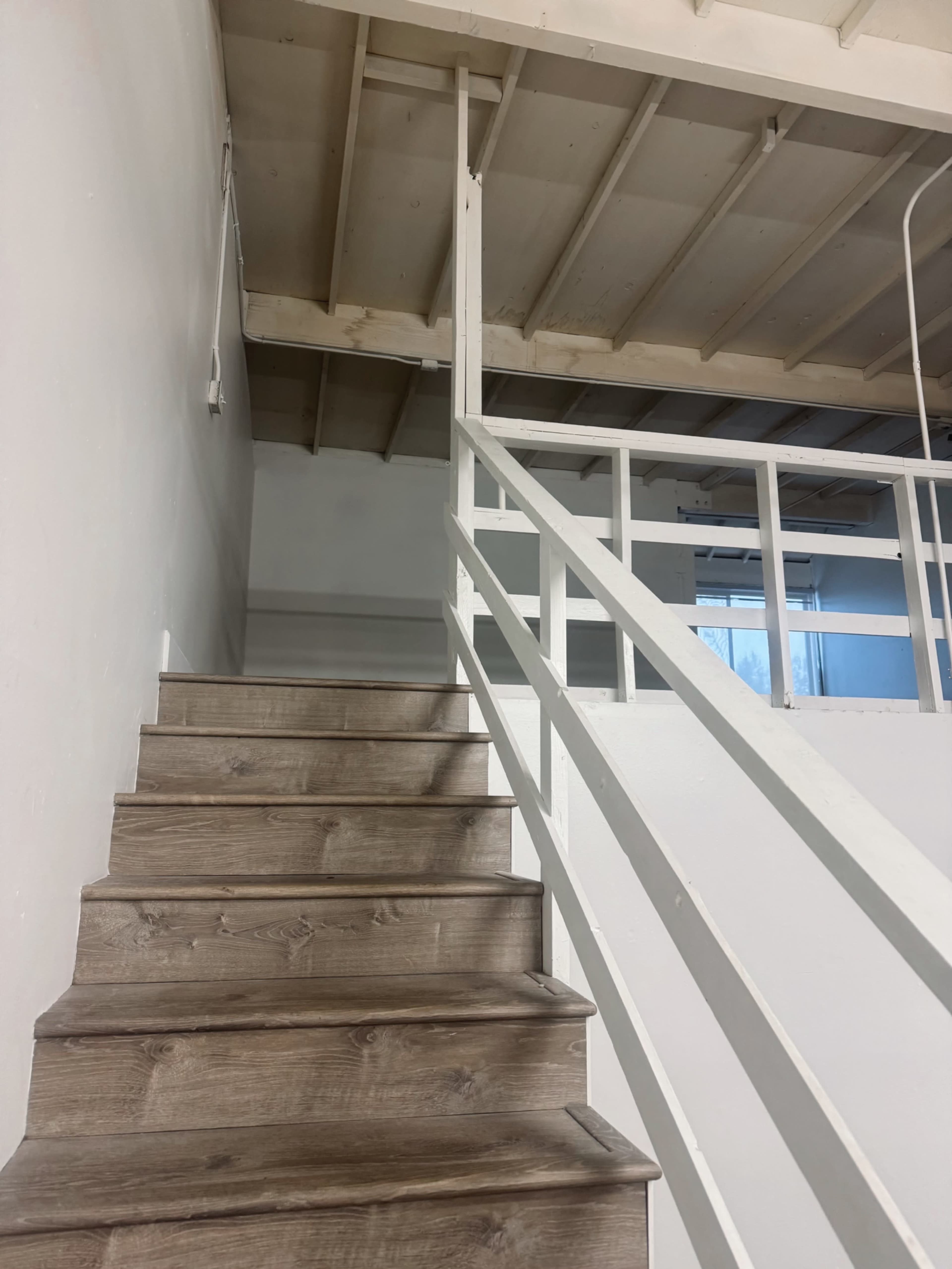 The image shows a set of wooden stairs leading upward to a landing with a white railing and a visible upper level.