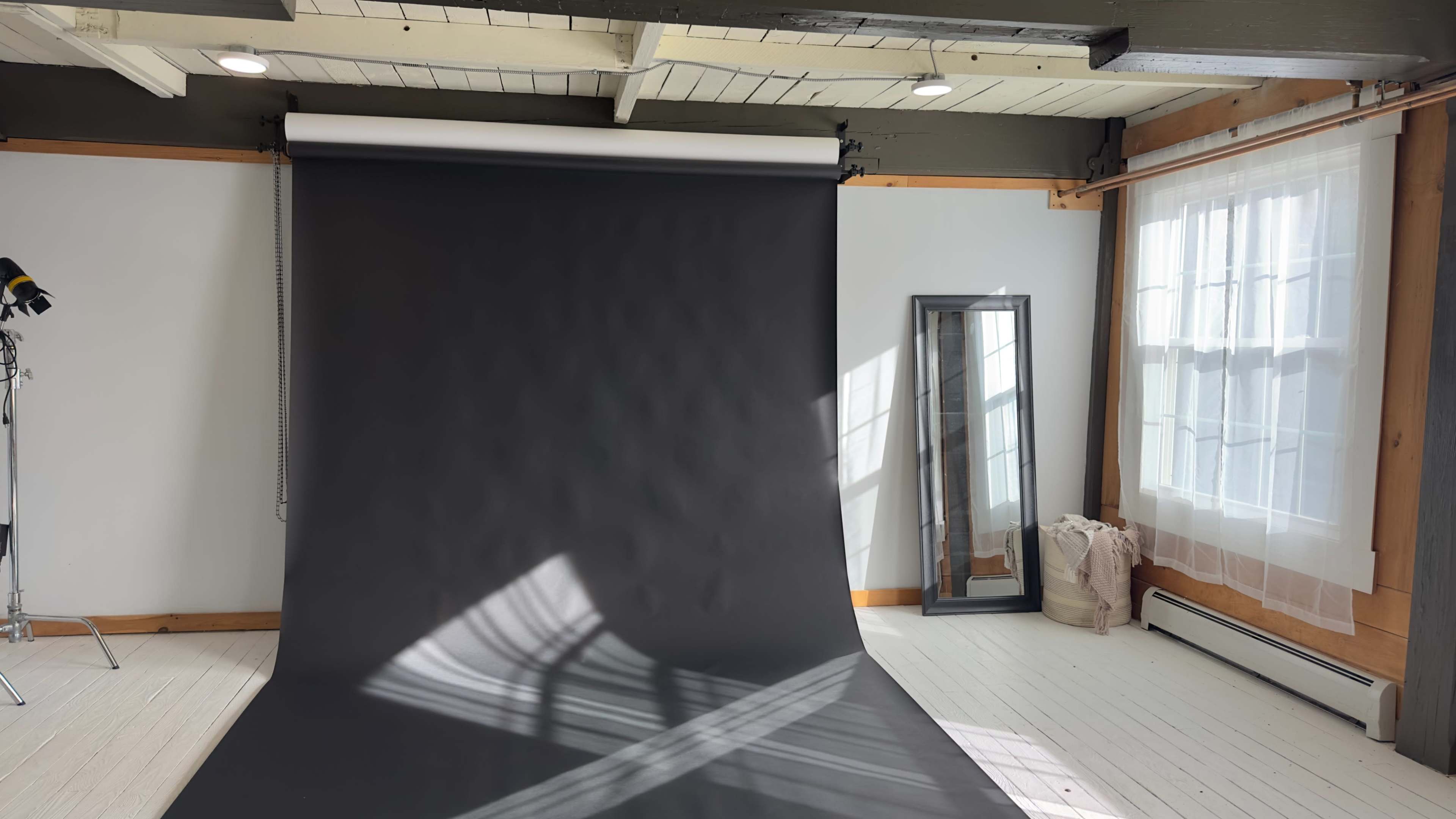The image shows a photography studio with a black backdrop, a mirror, and natural light streaming through a window.