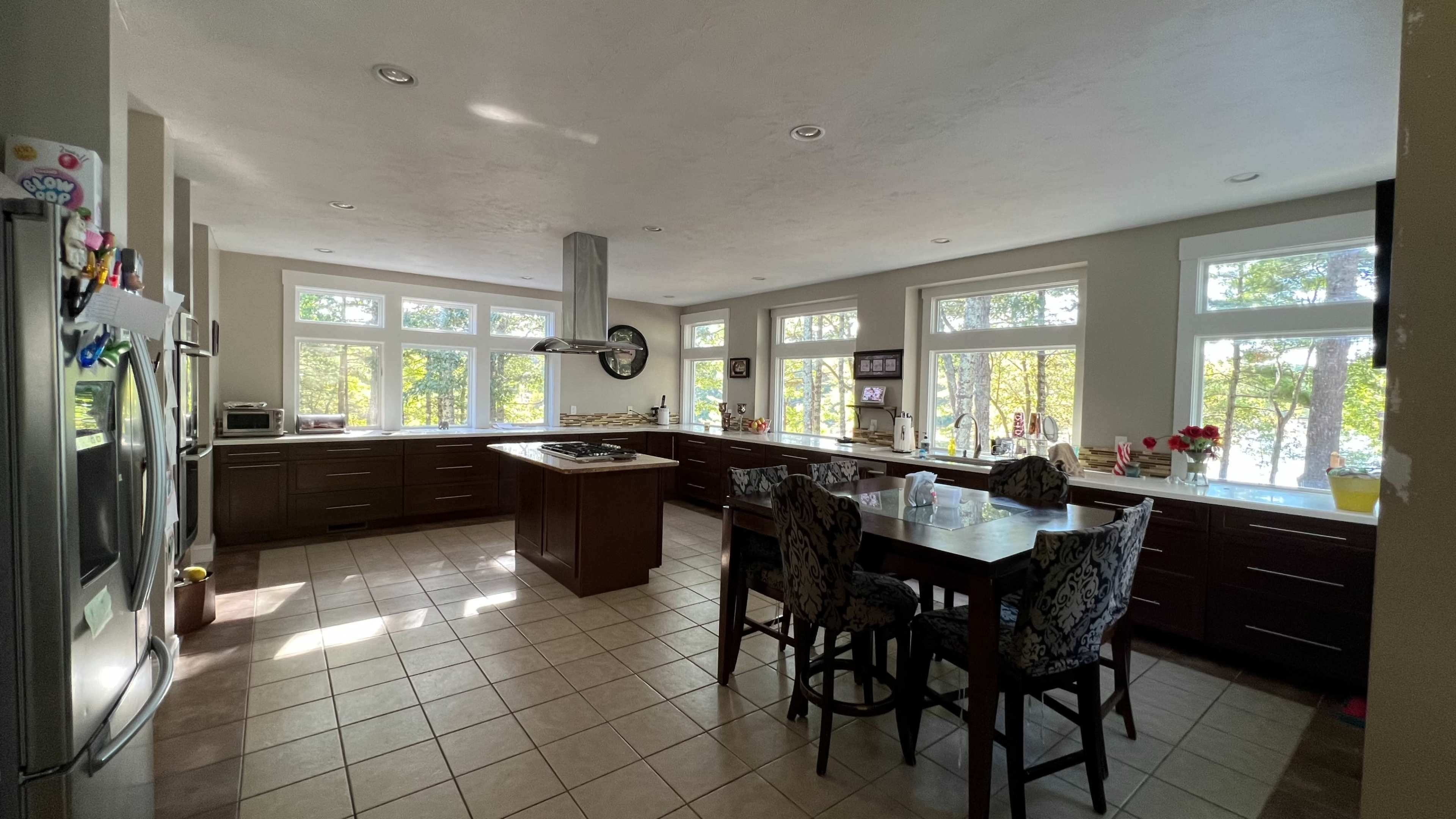 A spacious kitchen features large windows overlooking a natural landscape, with modern appliances and a central island.