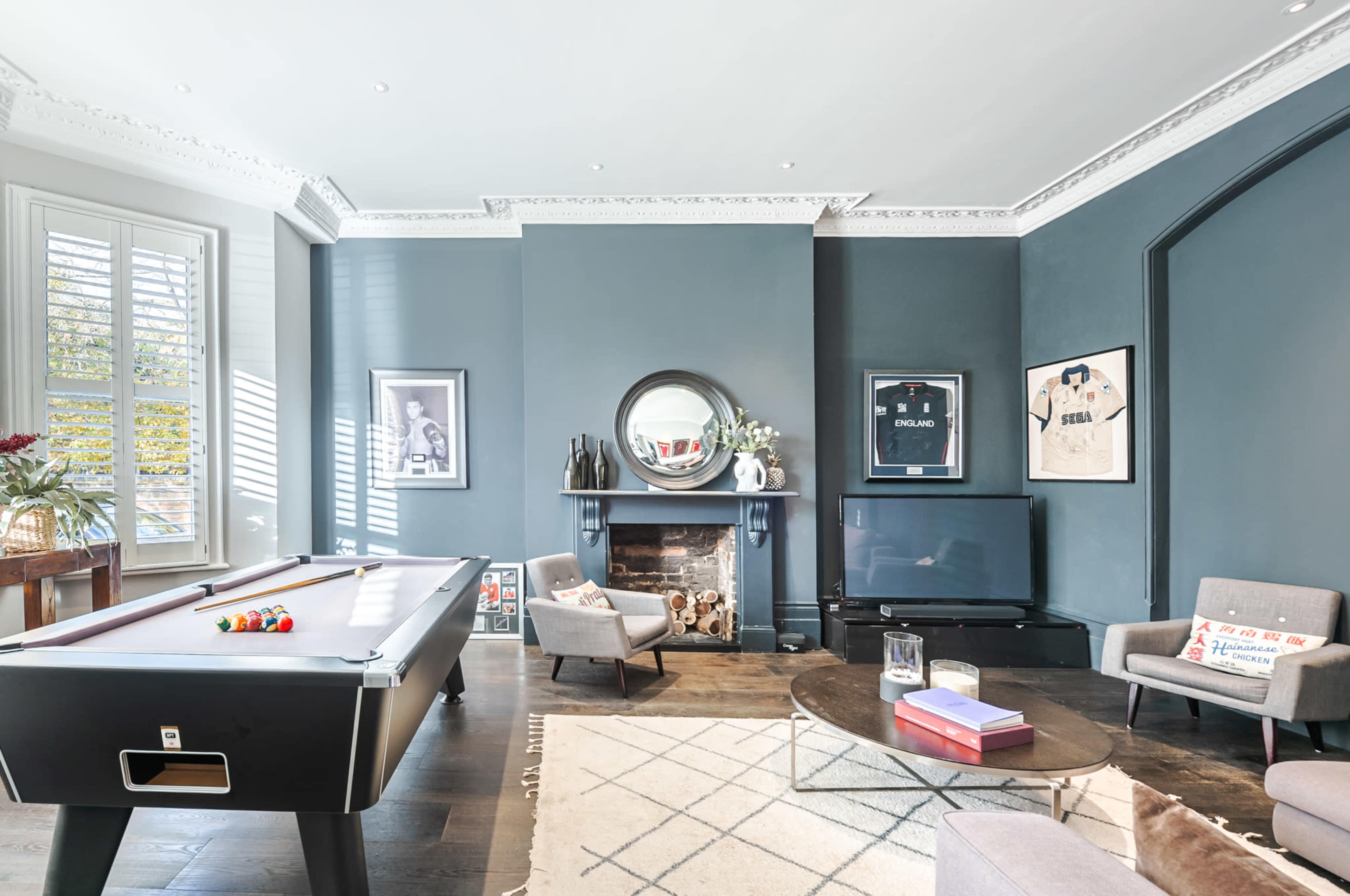 A stylish game room featuring a billiards table, a round coffee table, and an entertainment area with a fireplace and framed sports memorabilia on the walls.