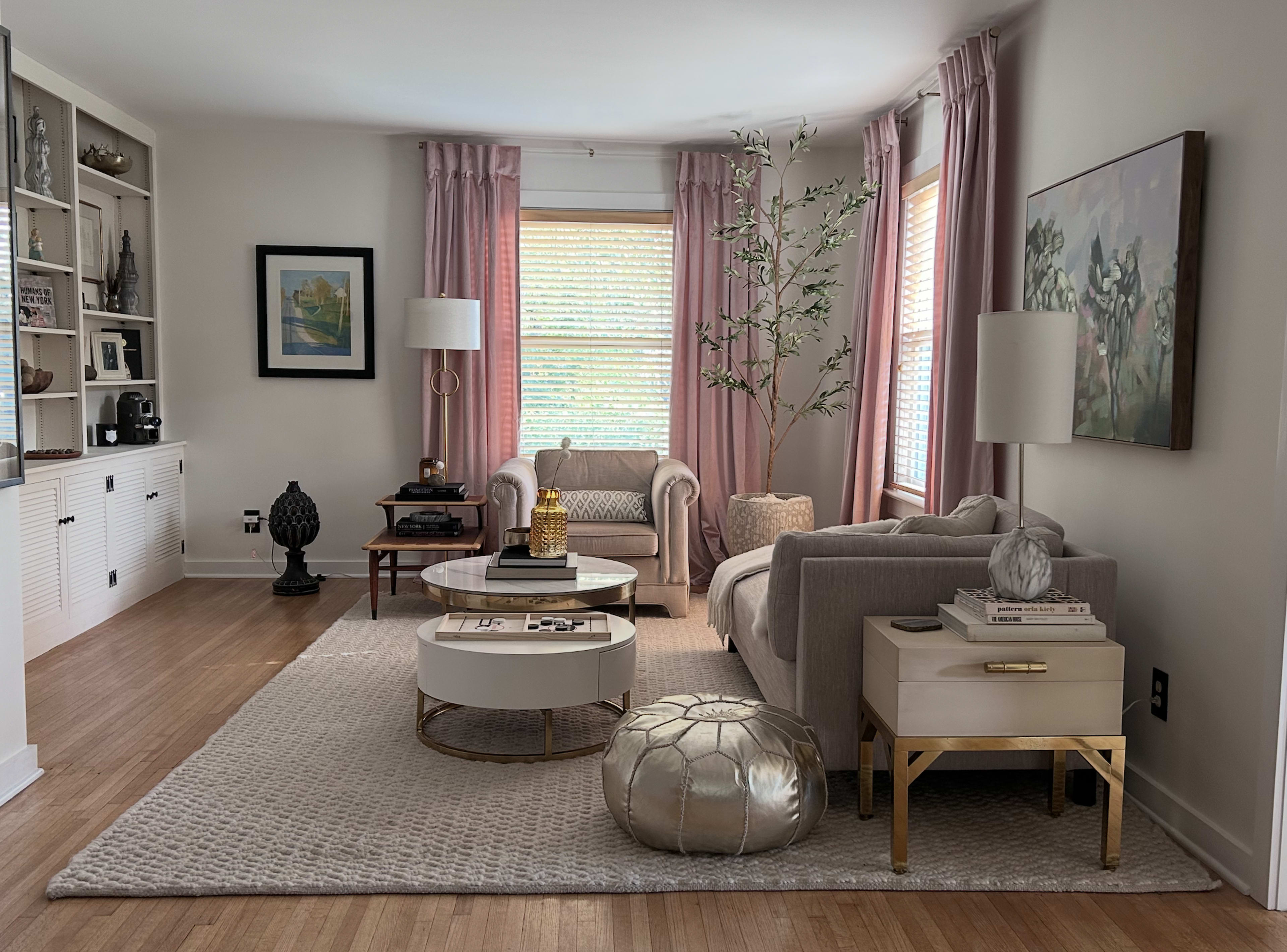 The living room features two sofas, a round coffee table, a plush area rug, curtains, a decorative plant, and various decorative items placed on shelves and tables.