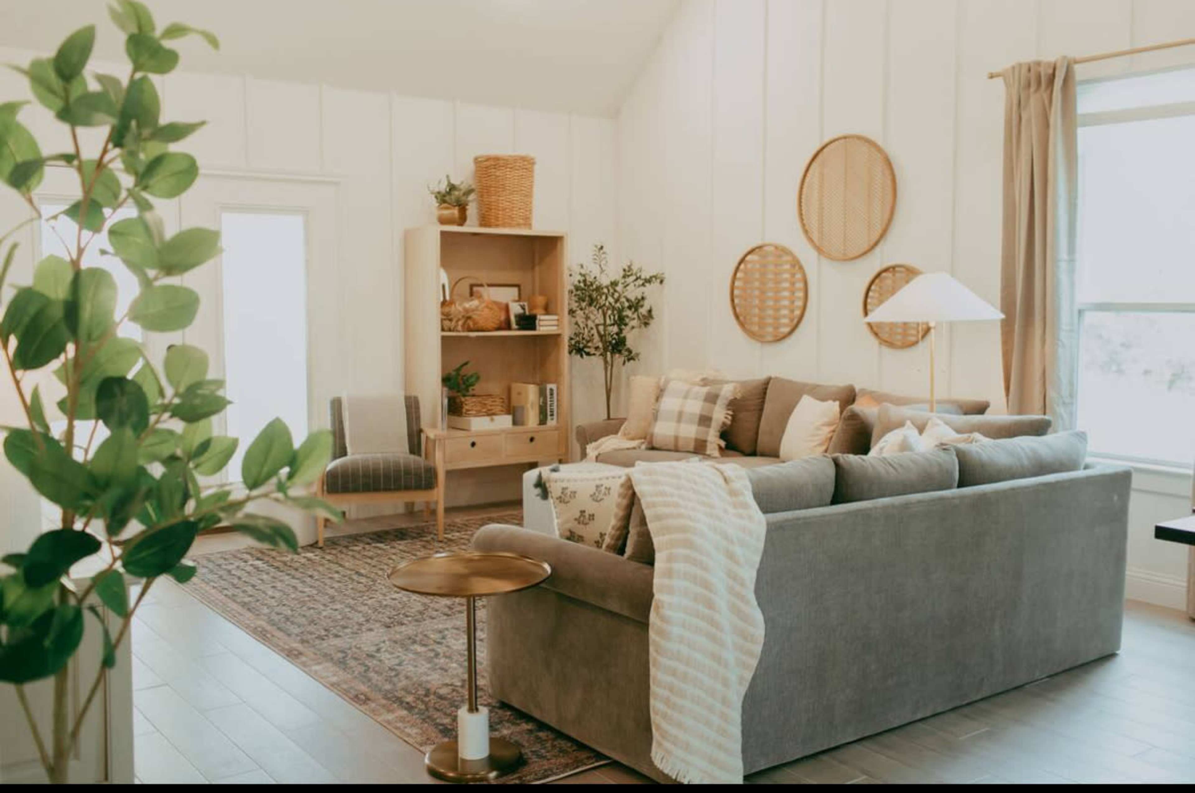 The image shows a cozy living room with a gray sofa, a decorative rug, a bookshelf, and natural light coming through the windows.