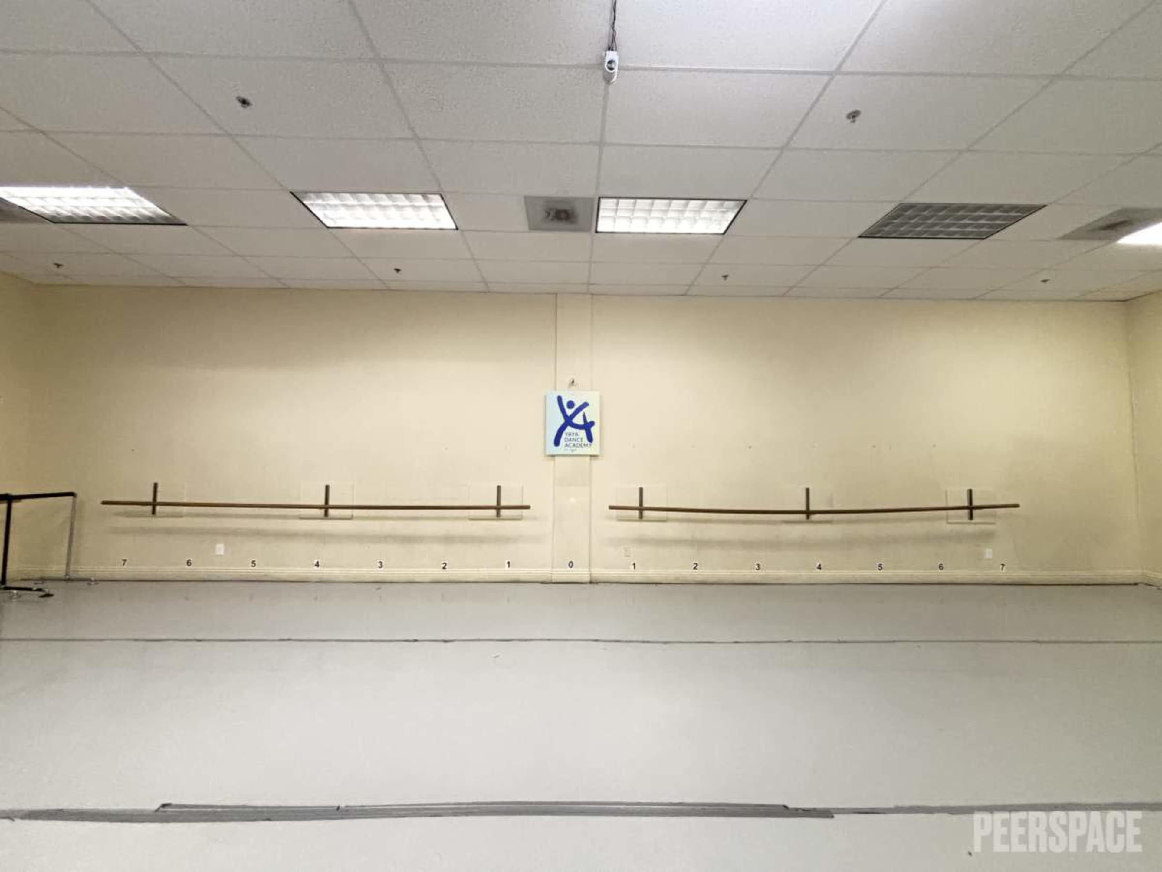 The image shows an empty dance studio with bare walls, a smooth floor, and a ballet barre along one side.
