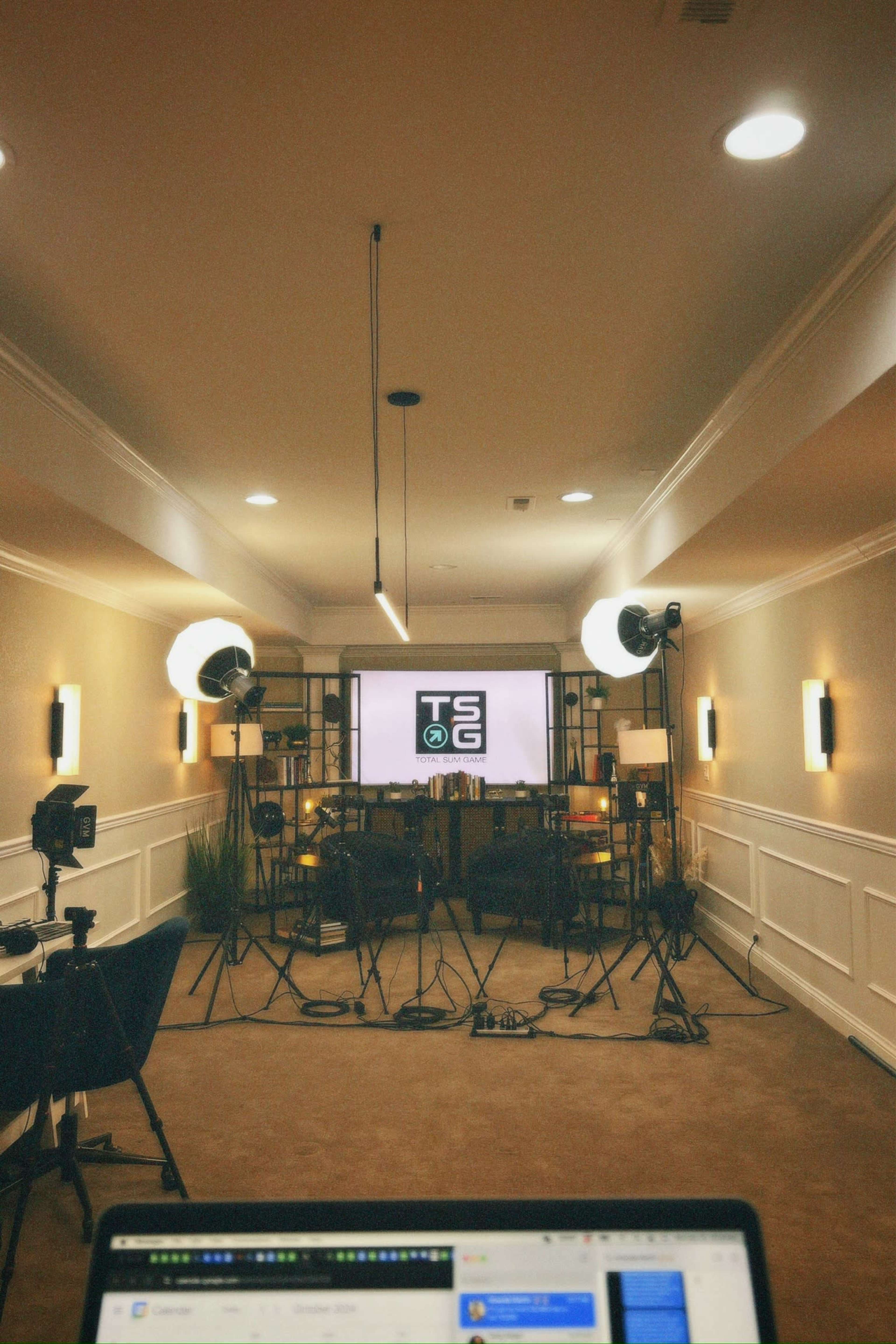 A well-lit studio space is set up for video production, featuring a large screen, cameras, and lighting equipment arranged around two chairs.