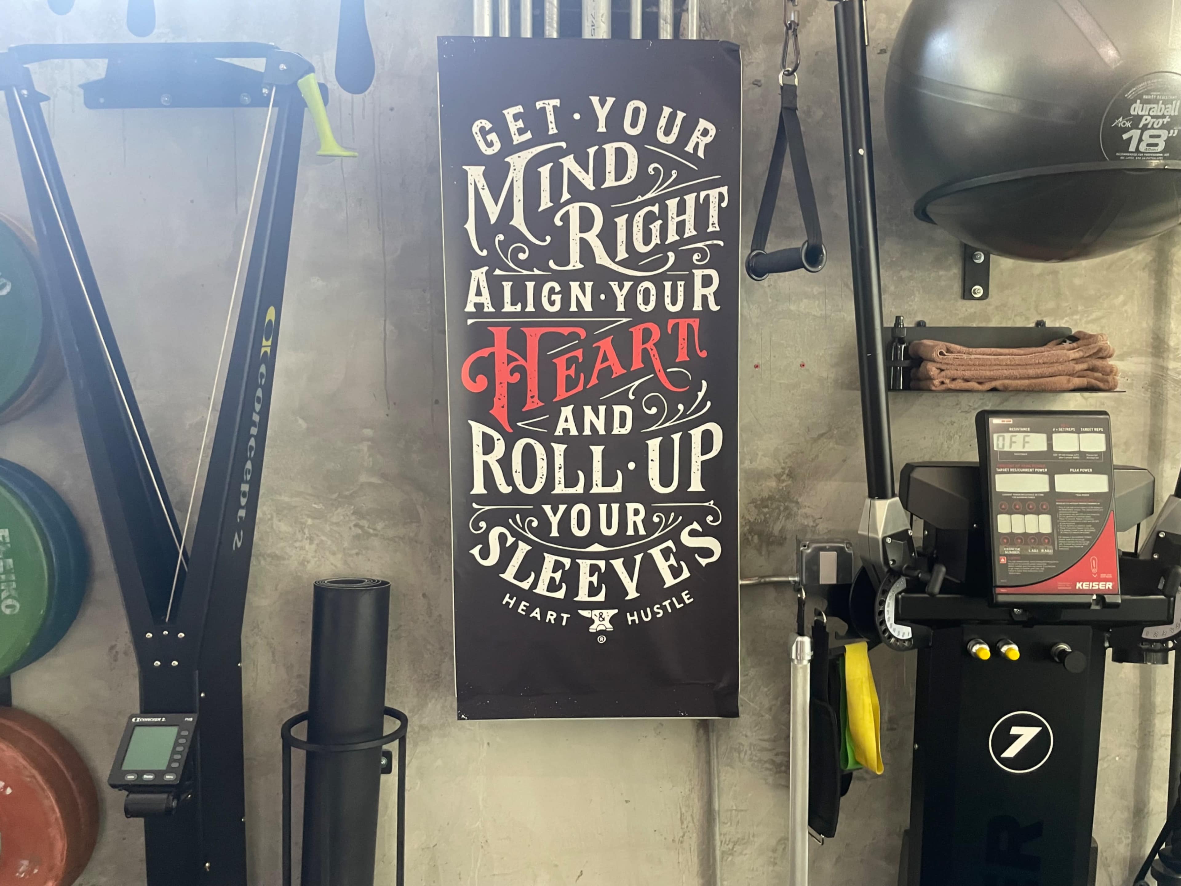 A motivational poster hanging on a wall in a gym, displaying the text "GET YOUR MIND RIGHT, ALIGN YOUR HEART, AND ROLL UP YOUR SLEEVES."